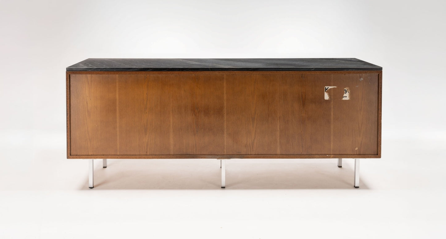 Mid-century Florence Knoll walnut credenza with black marble top and polished metal legs on white background.