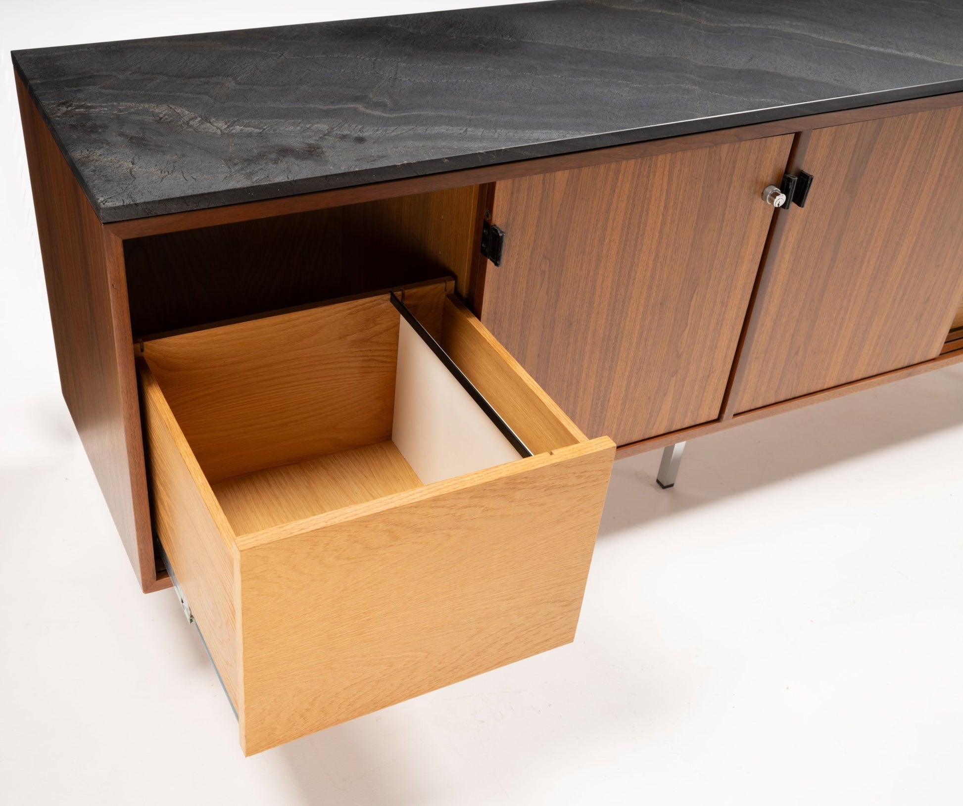 Mid-century walnut credenza with black marble top, four sliding doors, and open wooden drawer on white background.