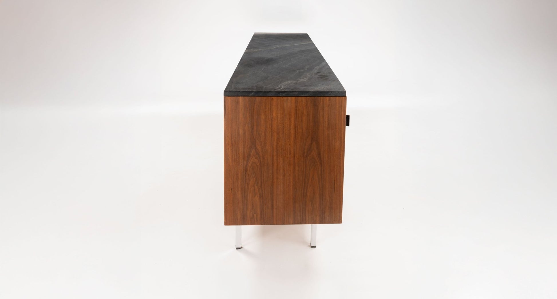 Side view of mid-century walnut Florence Knoll credenza with black marble top and polished metal legs on white background.
