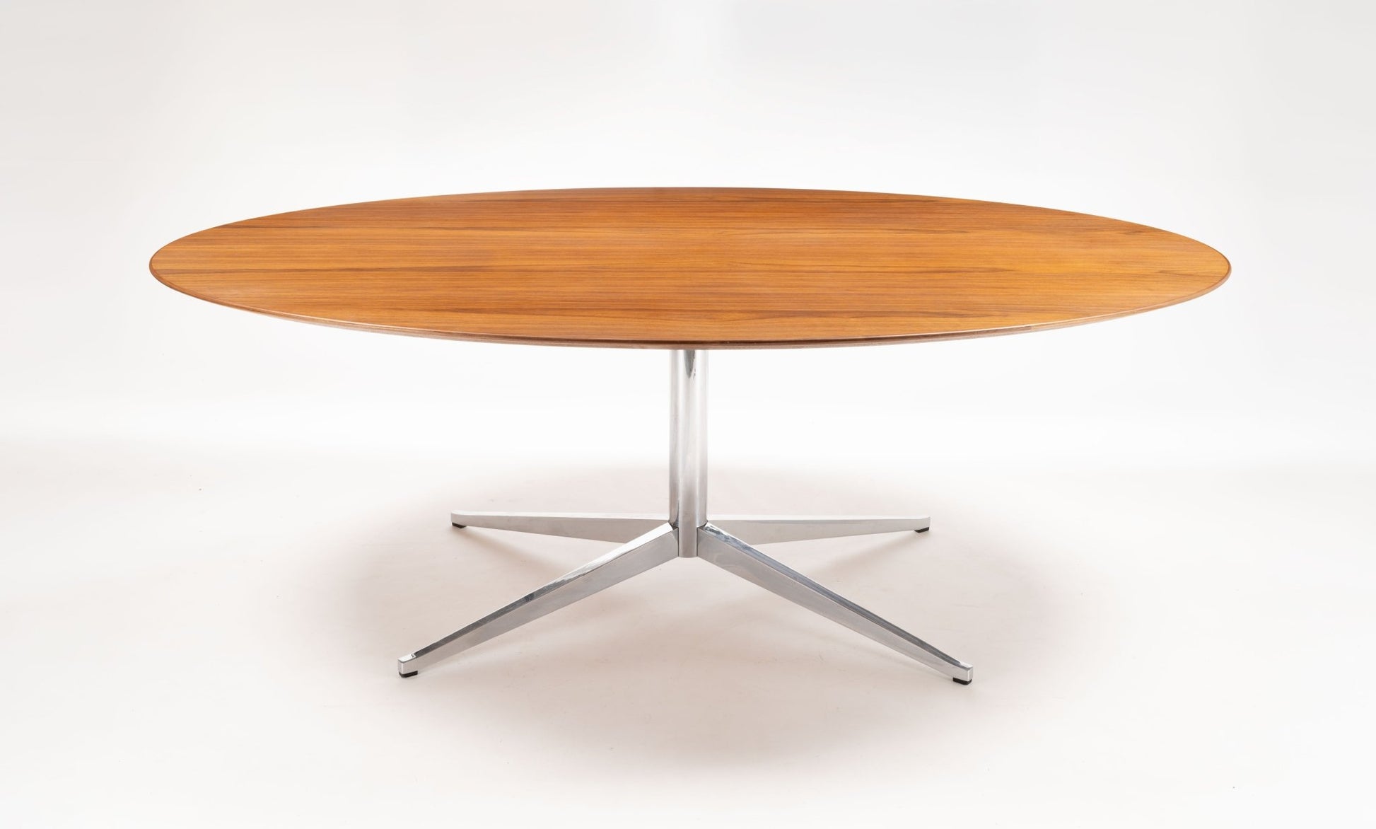 Mid-century modern Florence Knoll oval walnut dining table with polished chrome four-star base on white background