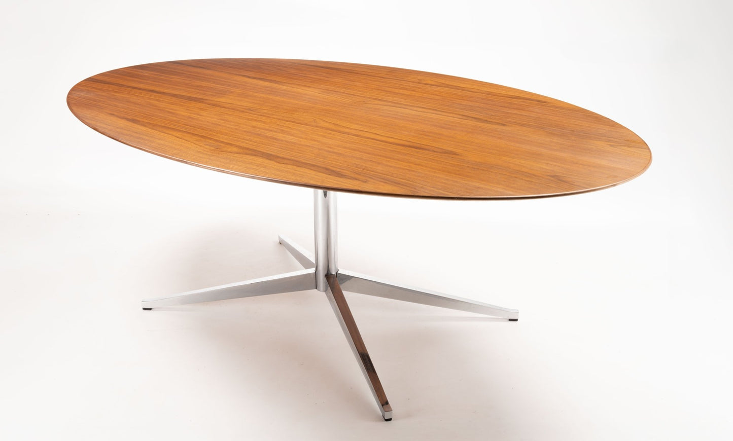 Florence Knoll oval dining table with walnut top and polished chrome four-star base on white background