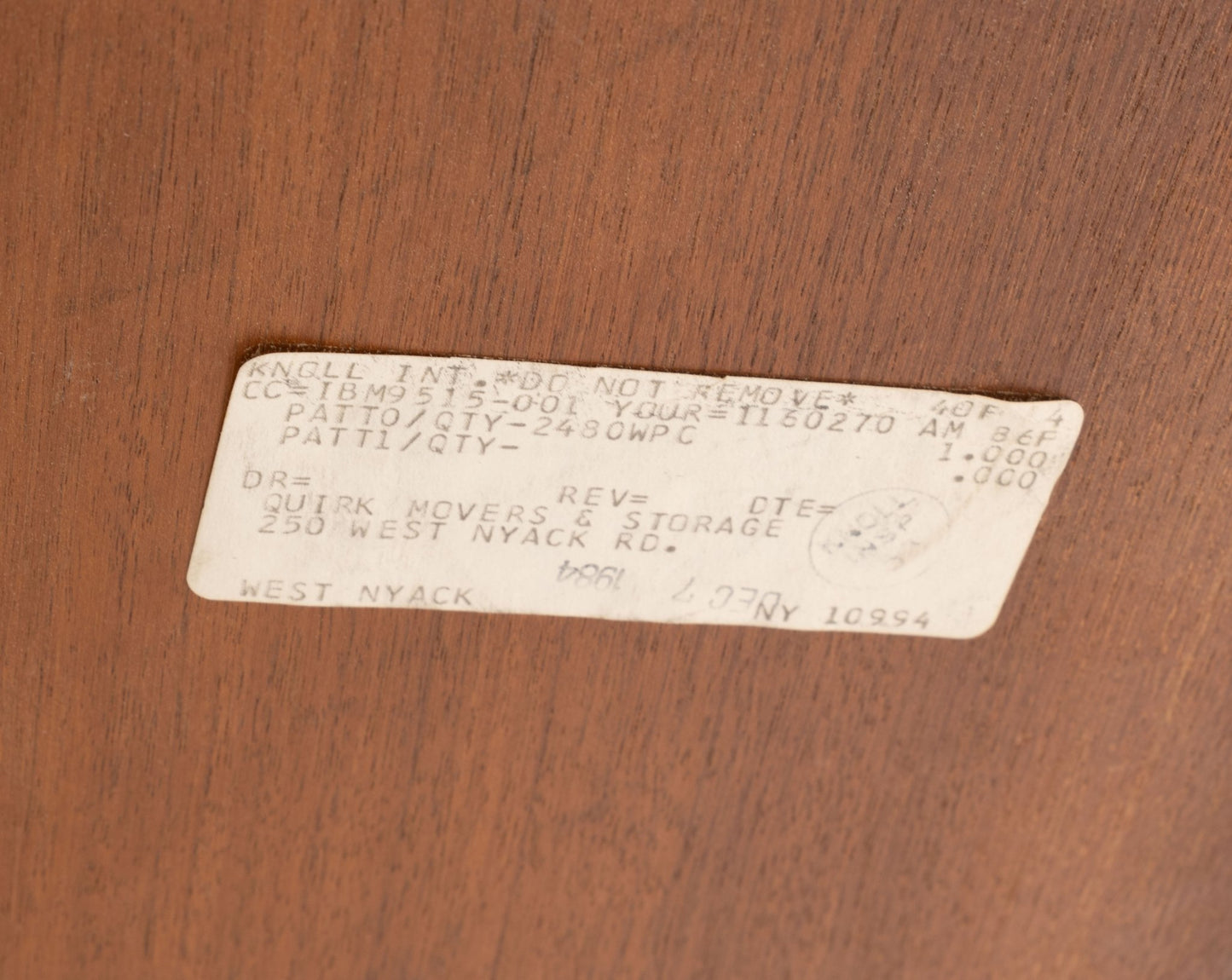 Close-up of vintage paper label on walnut surface of mid-century modern Florence Knoll oval dining table