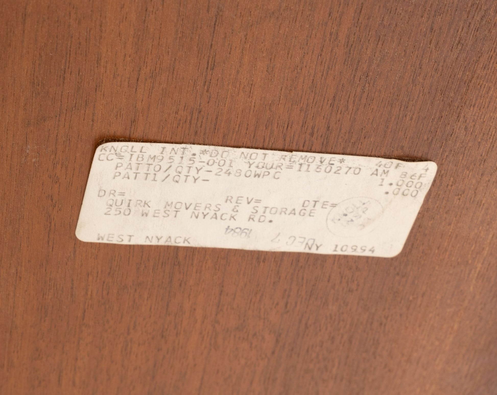 Close-up of vintage paper label on walnut surface of mid-century modern Florence Knoll oval dining table
