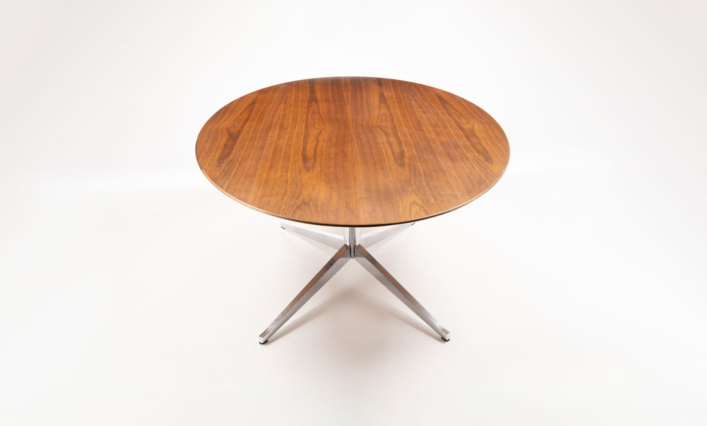 Oval mid-century modern walnut dining table with polished chrome four-star base on white background