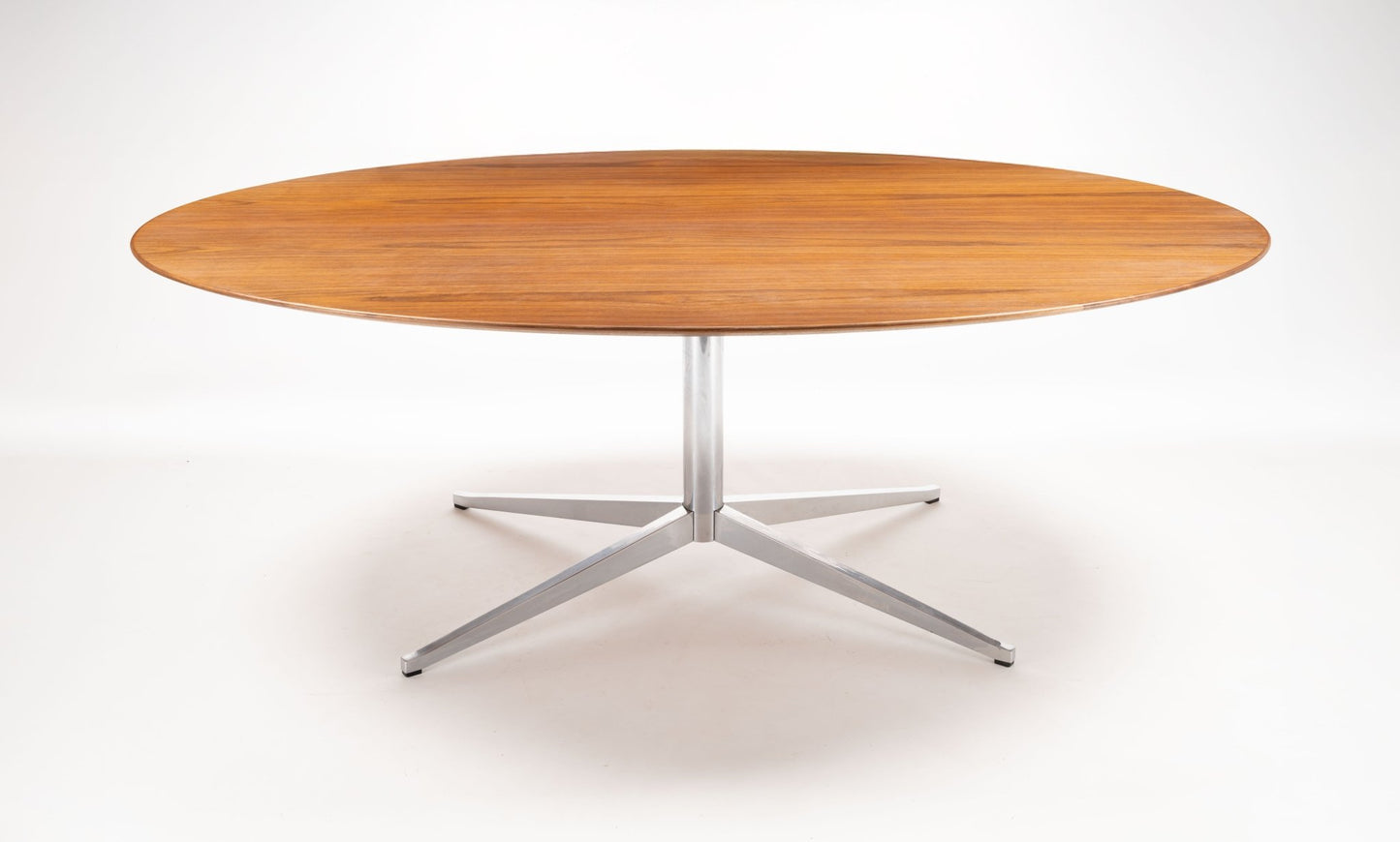 Oval mid-century modern walnut dining table with polished chrome four-star base on white background