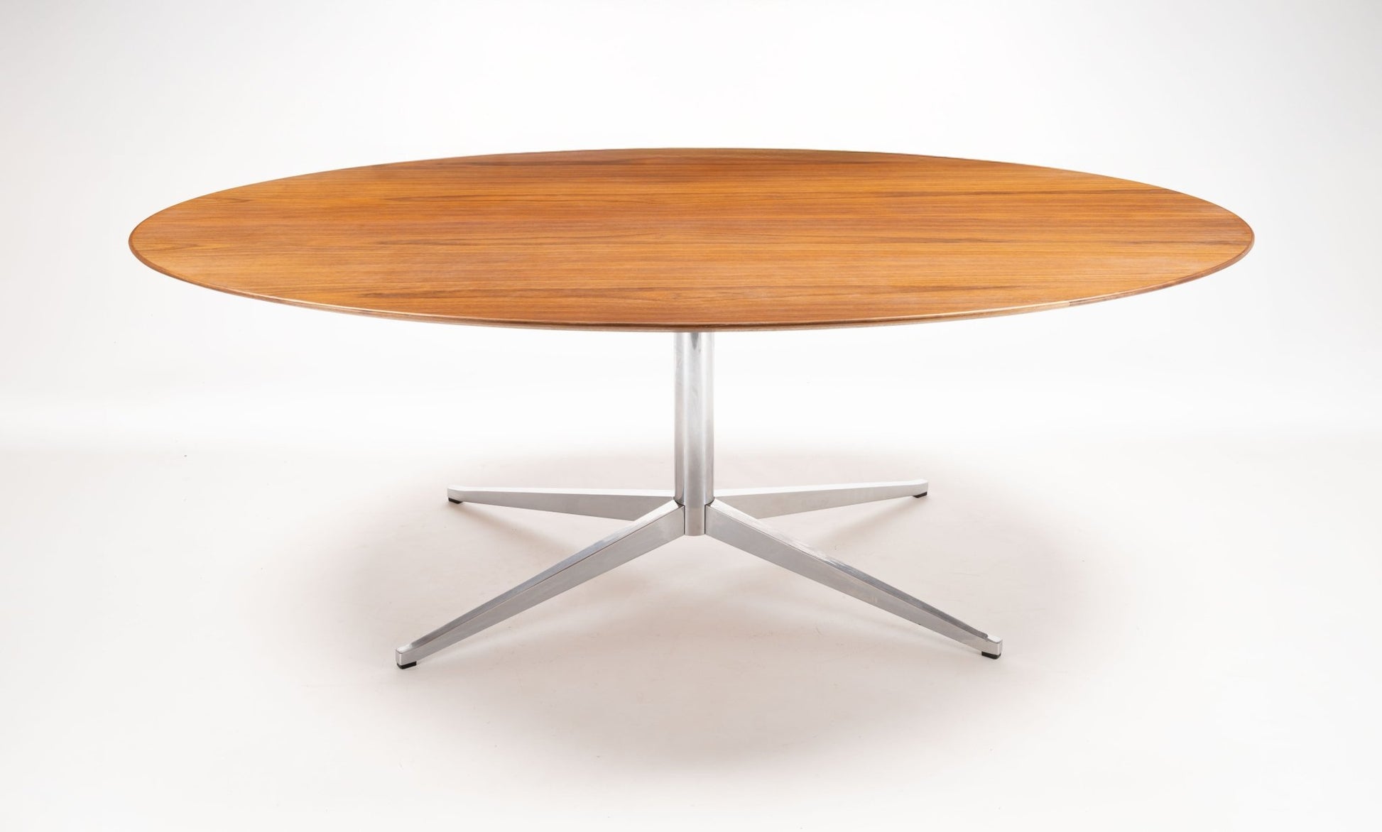 Oval mid-century modern walnut dining table with polished chrome four-star base on white background