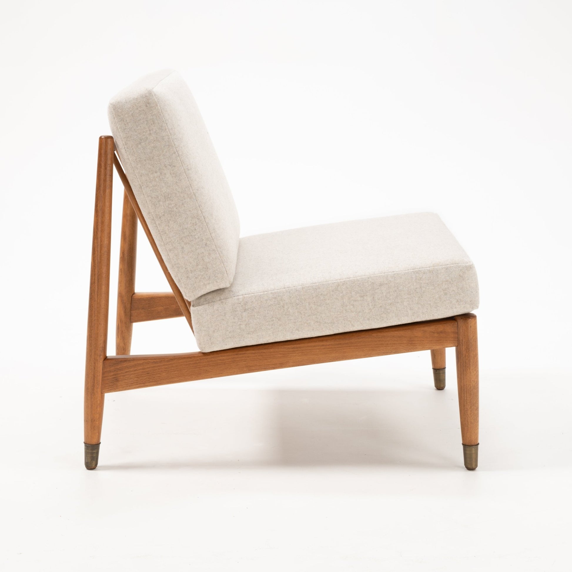 Side view of Folke Ohlsson slipper lounge chair with beige cushions and beechwood frame on white background