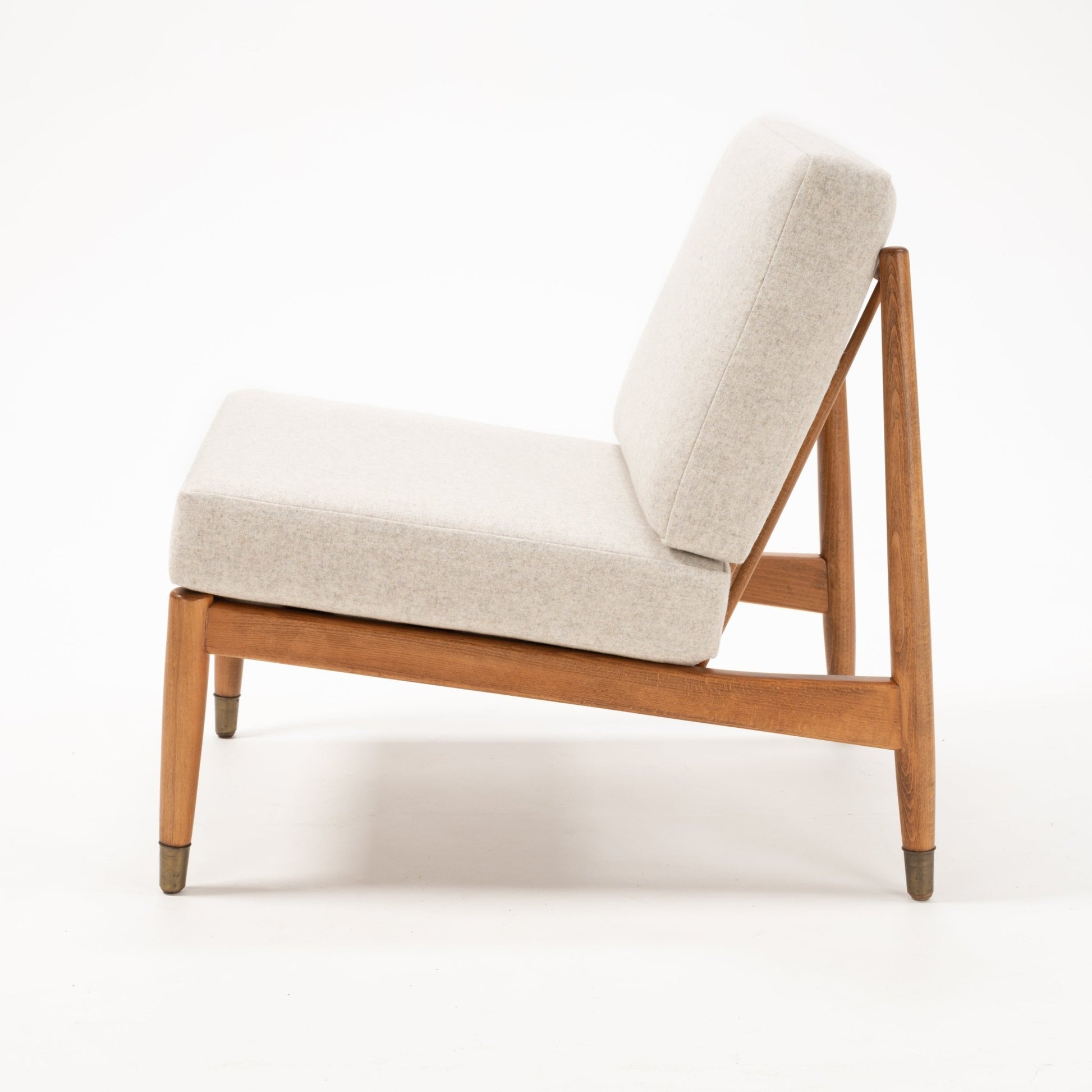 Side profile of Folke Ohlsson slipper lounge chair with beige cushions on a teak and beechwood frame against white background