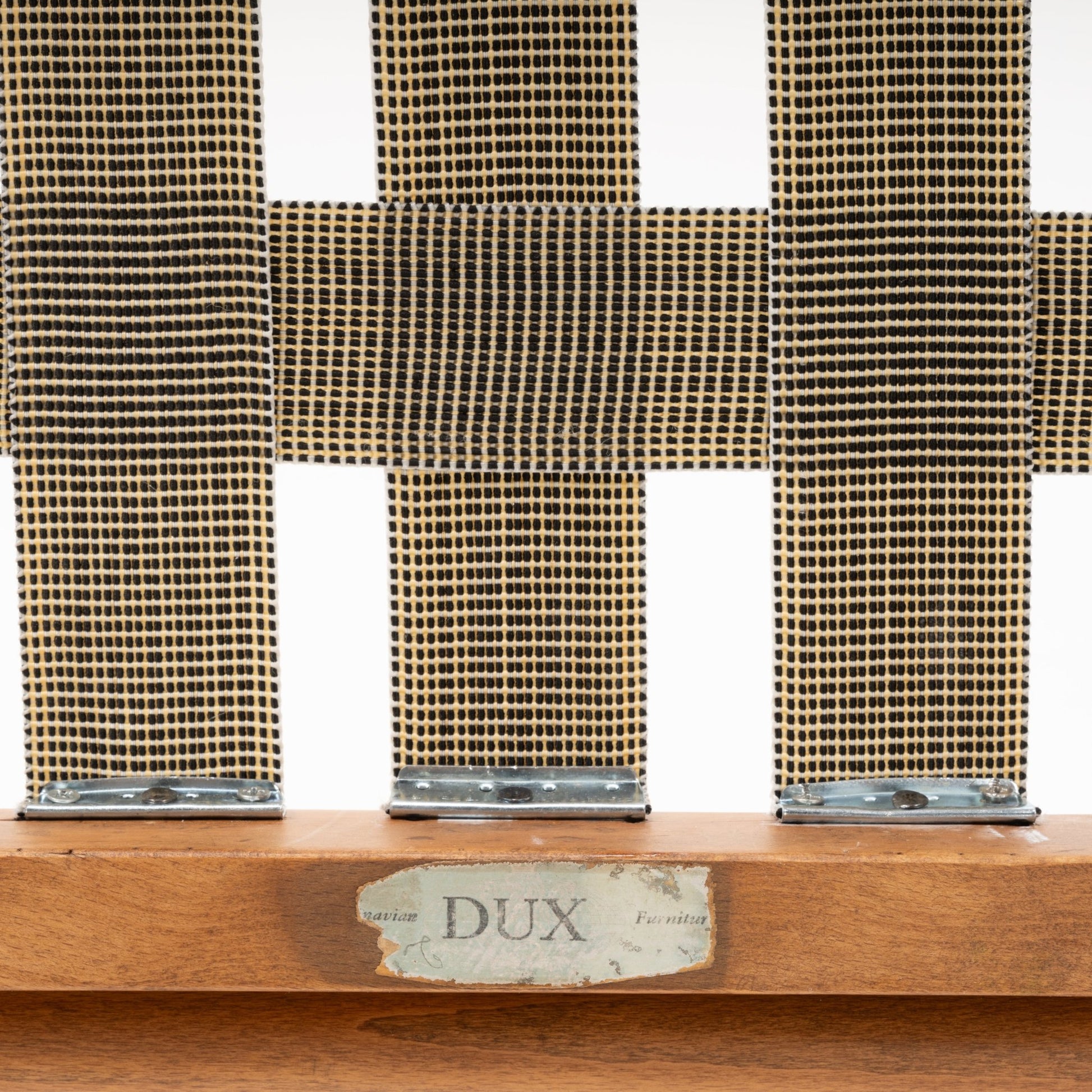 Close-up of woven seat webbing and vintage DUX label on warm-toned beechwood frame of slipper lounge chair