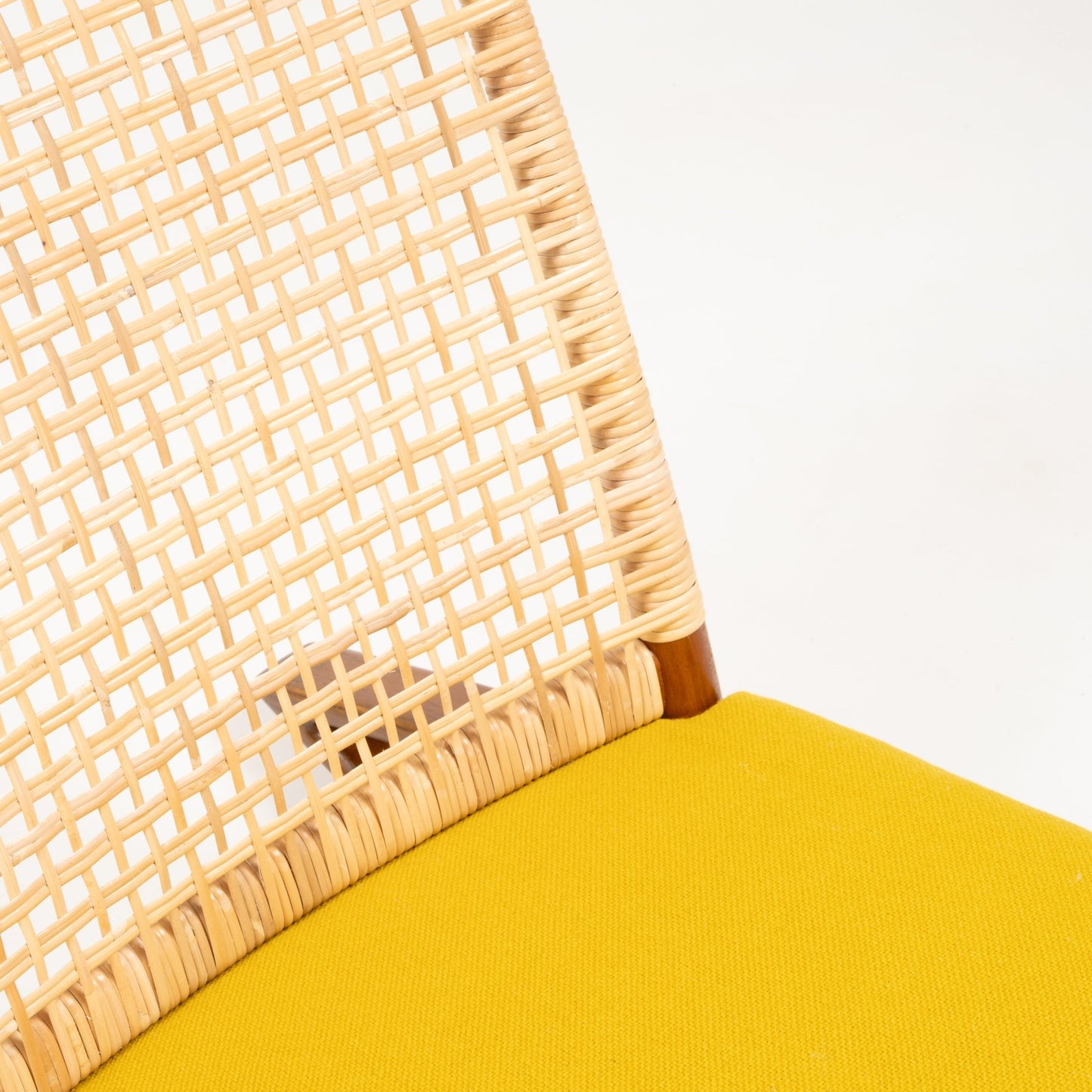 Close-up of woven cane backrest with smooth teak frame corner and mustard yellow wool cushion on white background