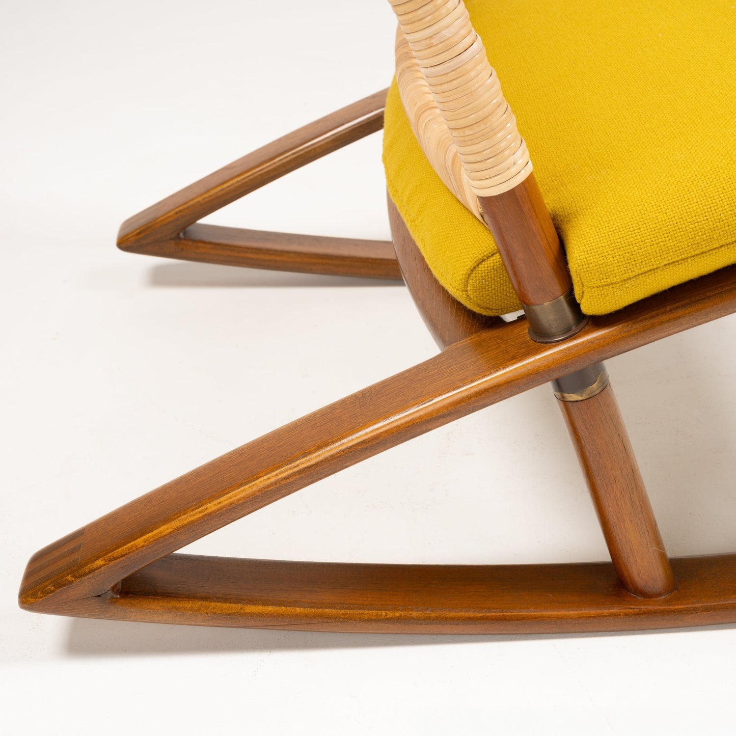 Close-up of polished teak rocker with woven armrest and mustard yellow wool cushion on white background