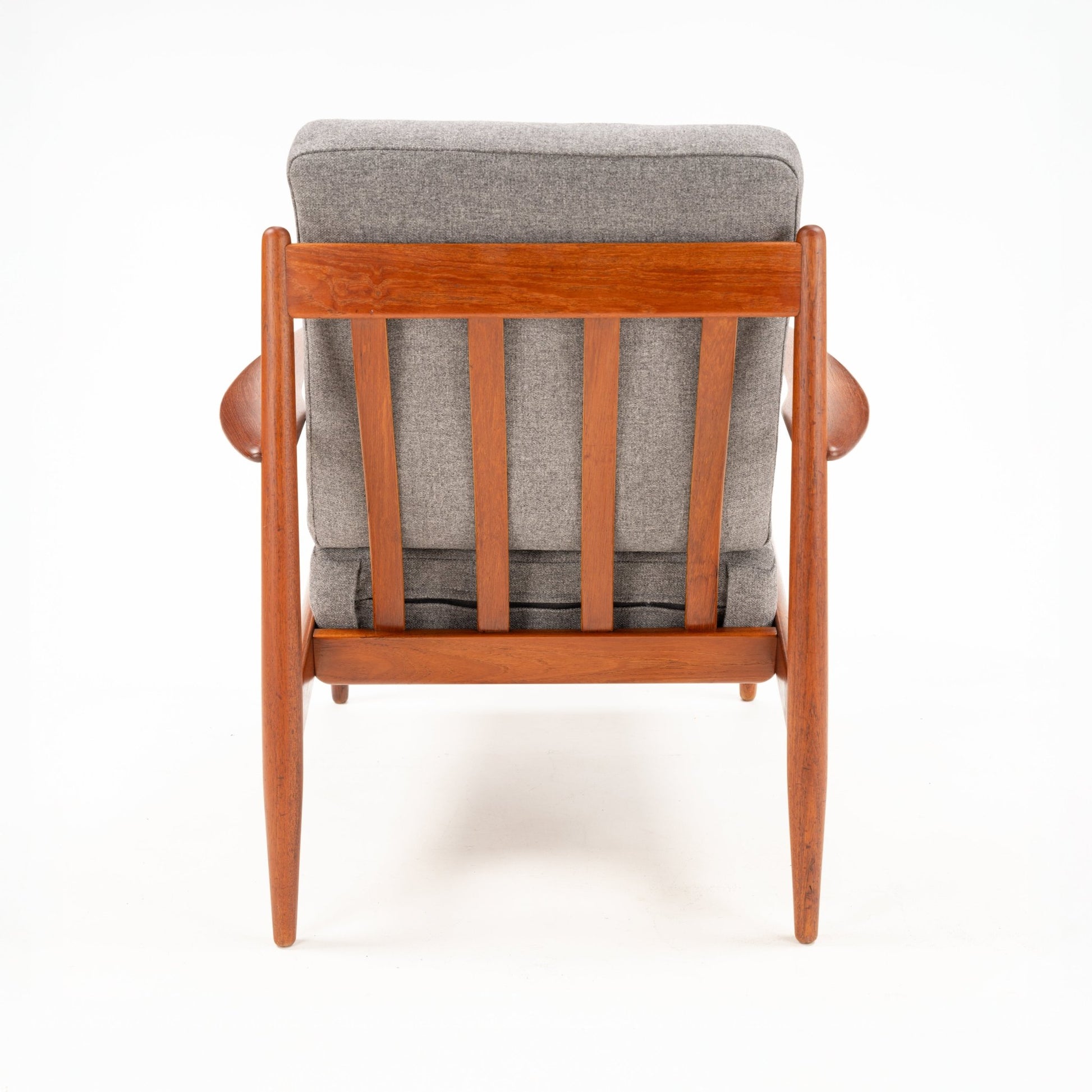 Rear view of a wooden armchair with vertical slats and thick gray fabric cushions against a white background