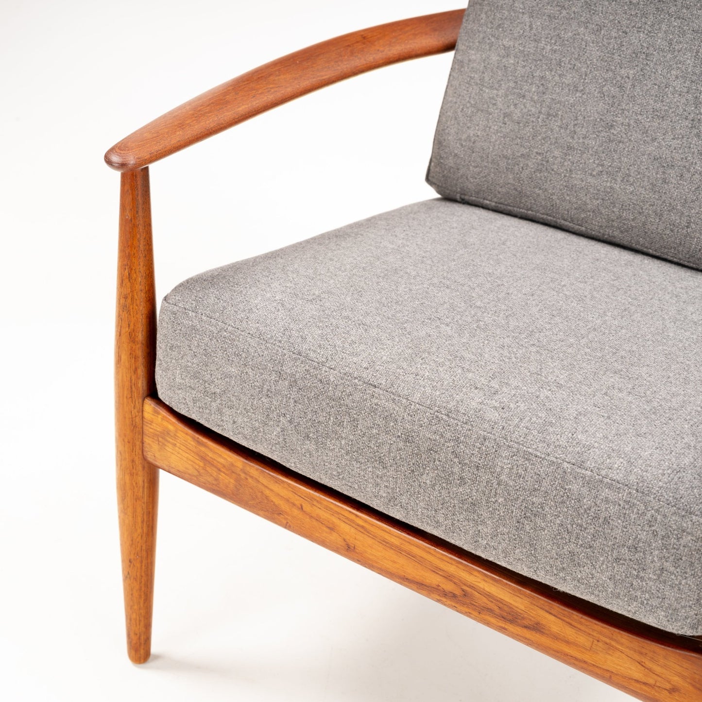 Close-up of a wooden armchair with curved armrest and thick gray fabric cushions on seat and backrest