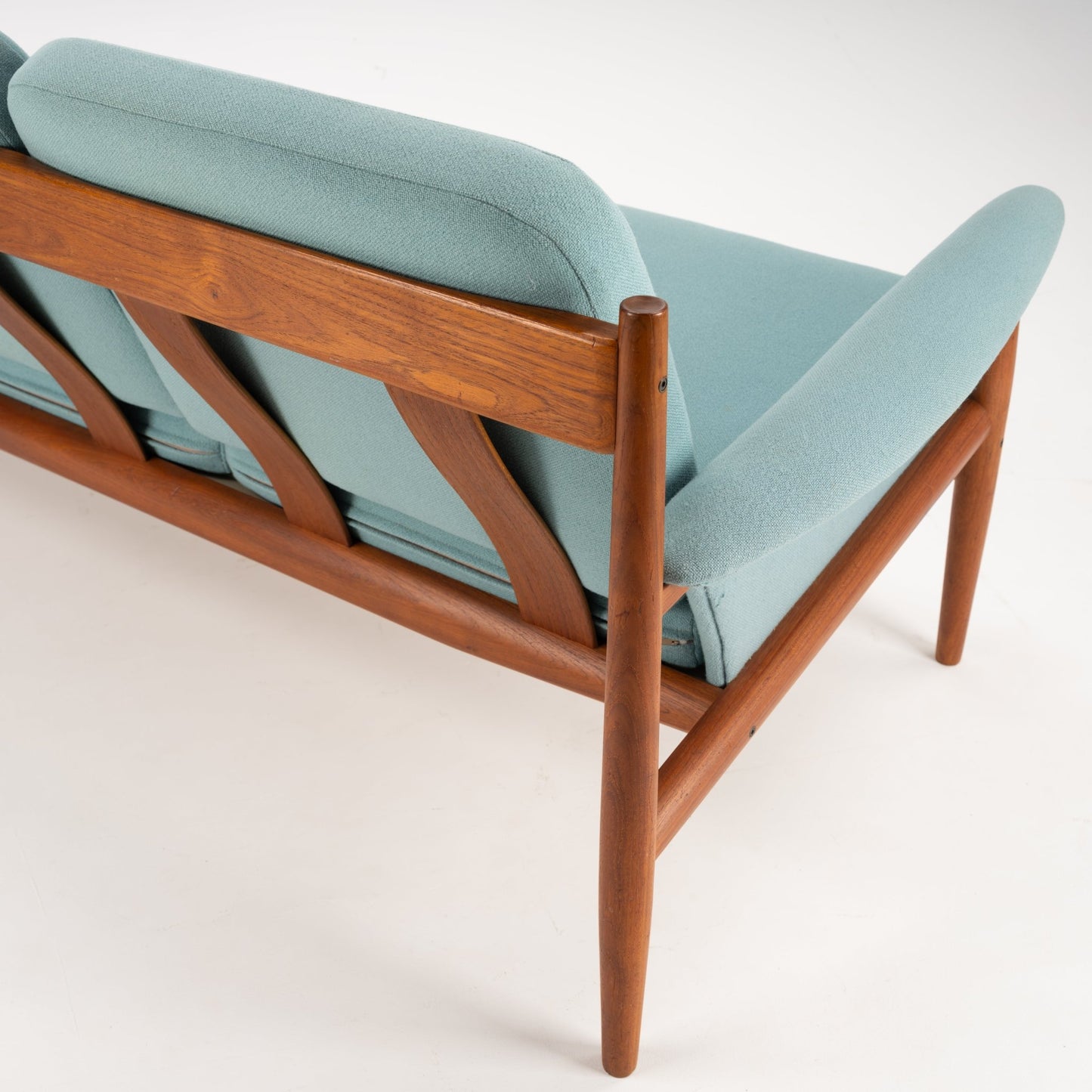 Grete Jalk Model 118 Teak Sofa showcasing a rich teak frame with elegantly angled supports and tapered legs, upholstered in soft muted seafoam fabric, reflecting mid century modern seating design.