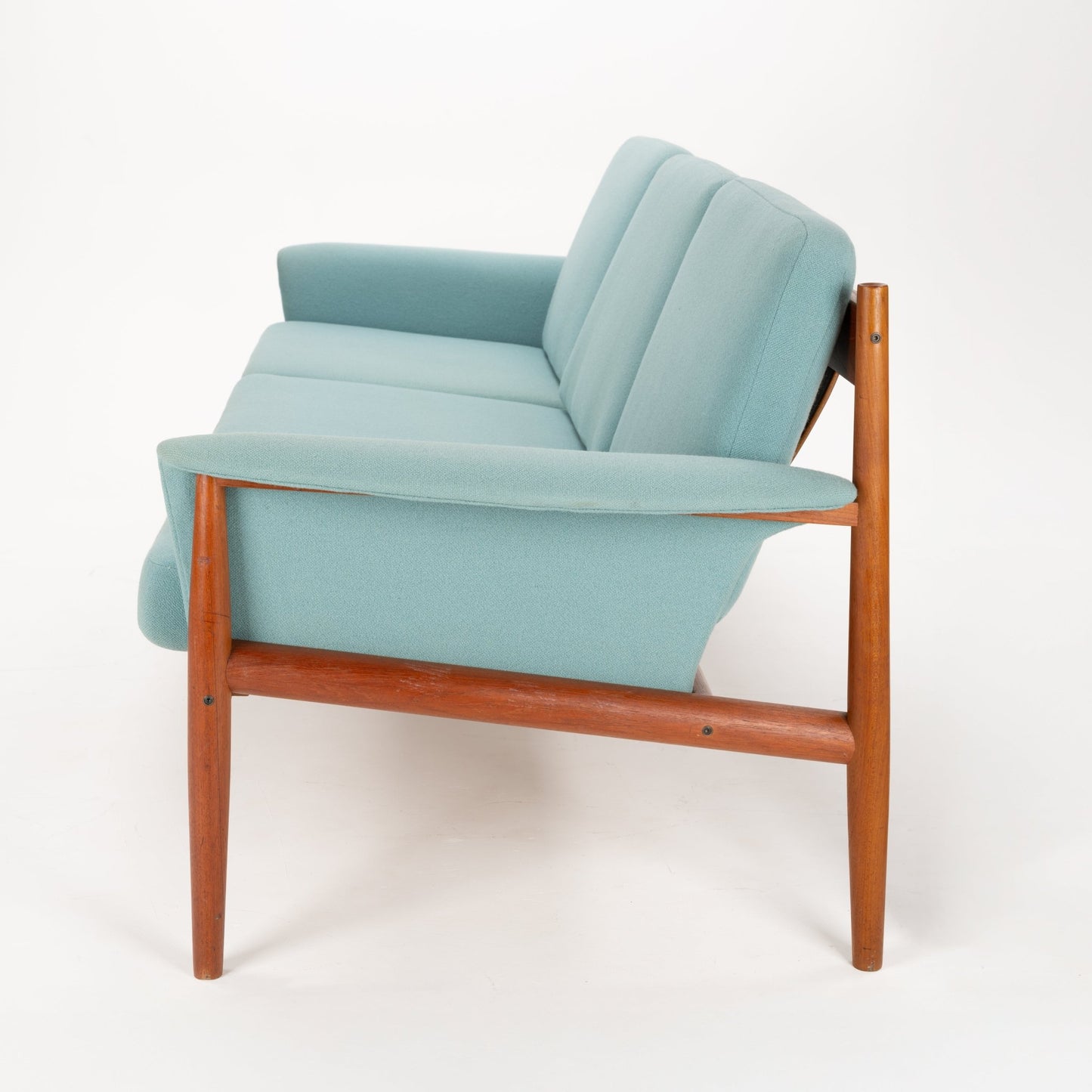 Grete Jalk Model 118 Teak Sofa with a warm teak frame featuring slender legs and armrests, upholstered in soft pastel blue fabric, offering refined mid century modern seating.