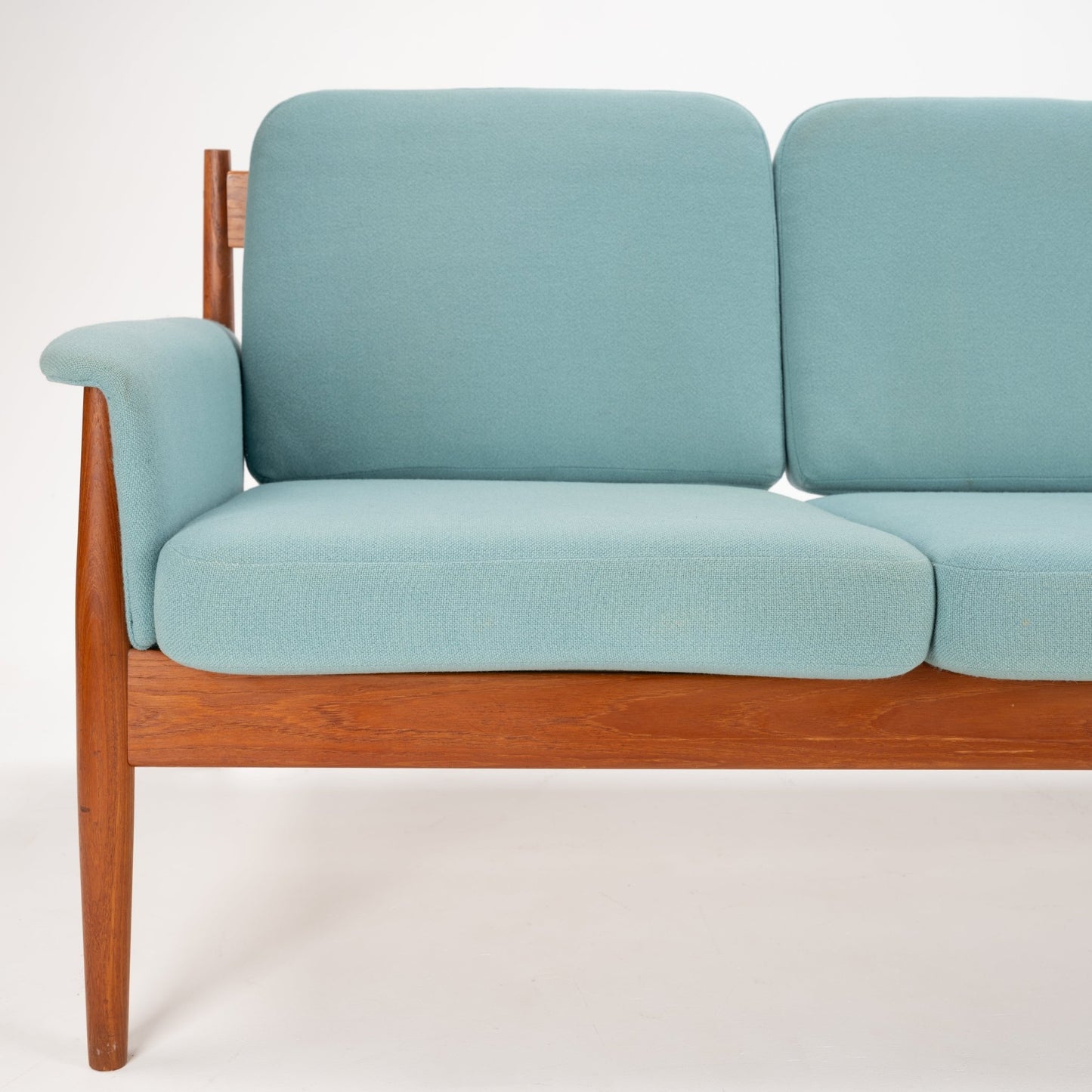 Grete Jalk Model 118 Teak Sofa featuring a warm teak frame with slender legs and armrests, paired with soft pastel blue cushions for elegant mid century modern seating.