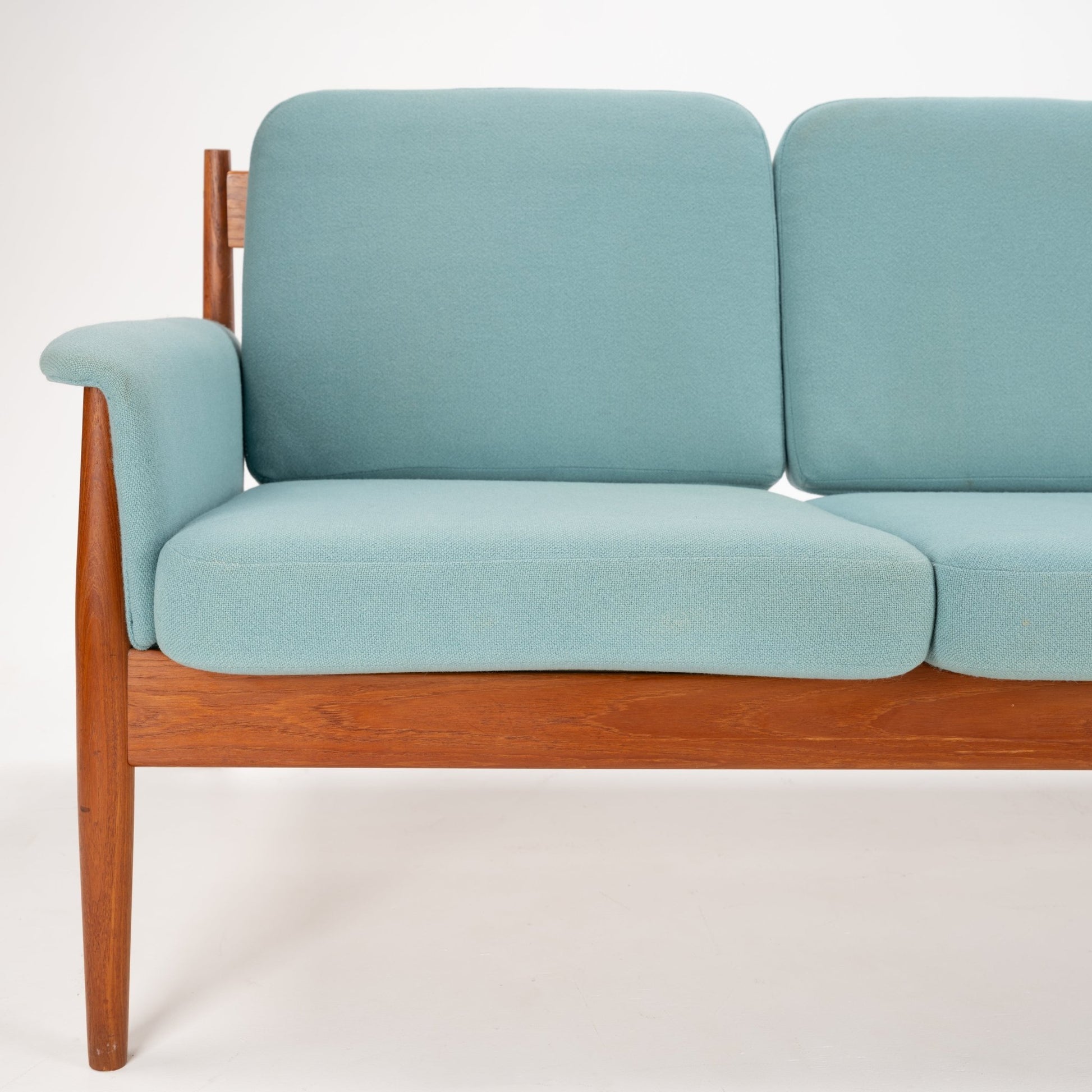 Grete Jalk Model 118 Teak Sofa featuring a warm teak frame with slender legs and armrests, paired with soft pastel blue cushions for elegant mid century modern seating.