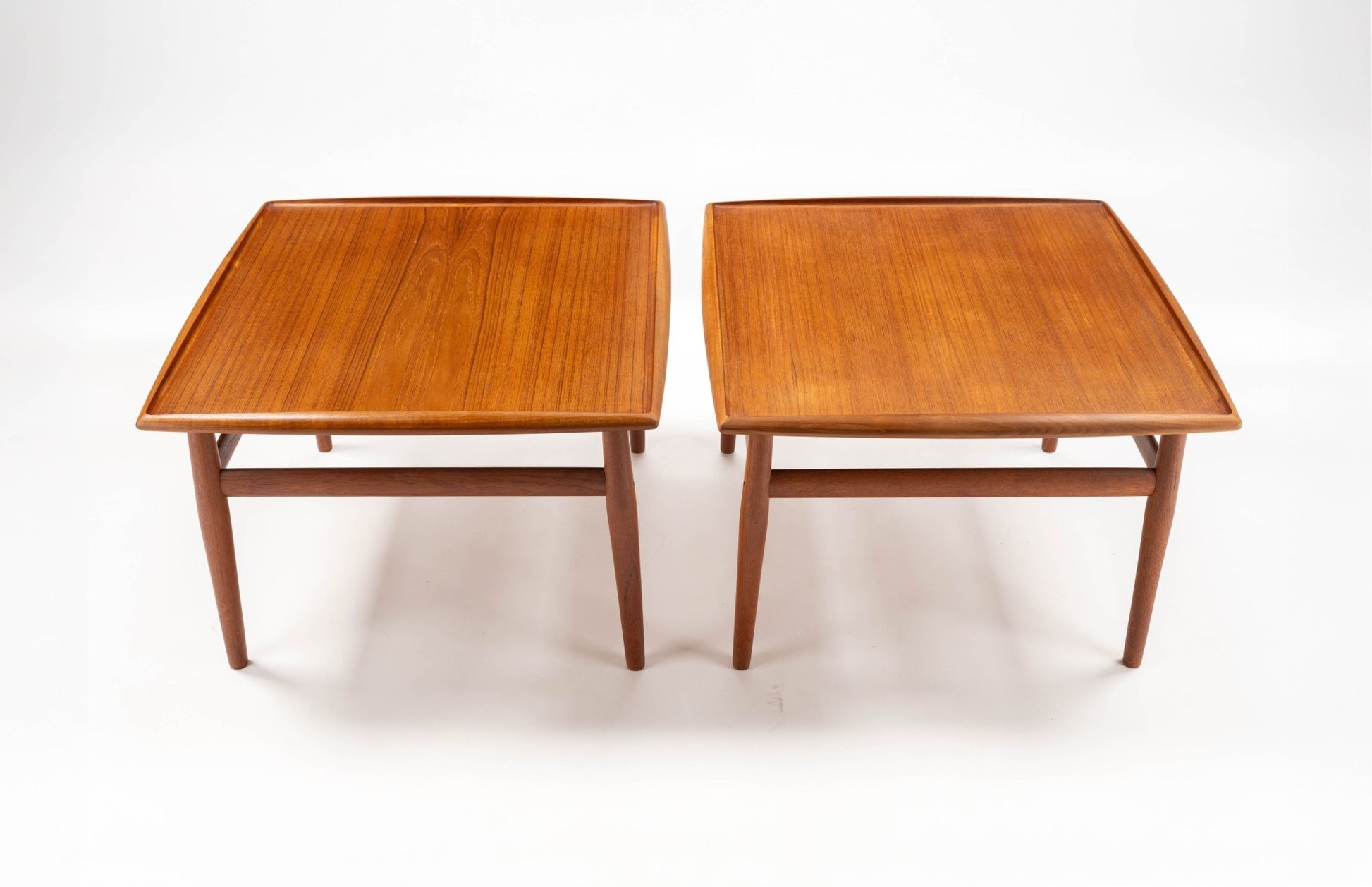 Pair of Grete Jalk Danish teak side tables with square tops, raised edges, turned legs, and stretcher supports