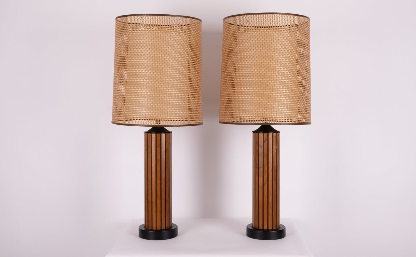 Pair of vintage 1960s walnut fluted wood table lamps with cane shades and black accents, featuring center diffusers.