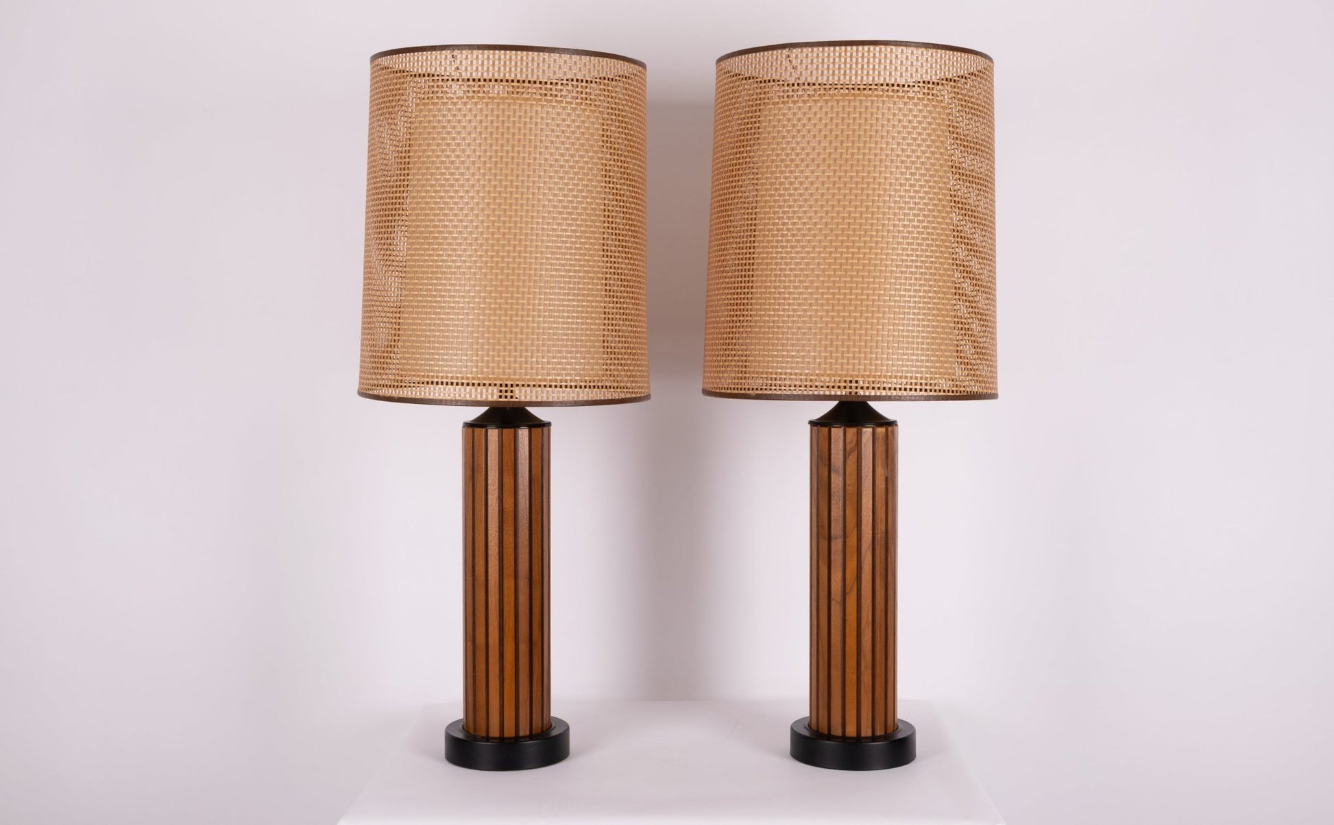 Pair of vintage 1960s walnut fluted wood table lamps with cane shades and black accents, featuring center diffusers.