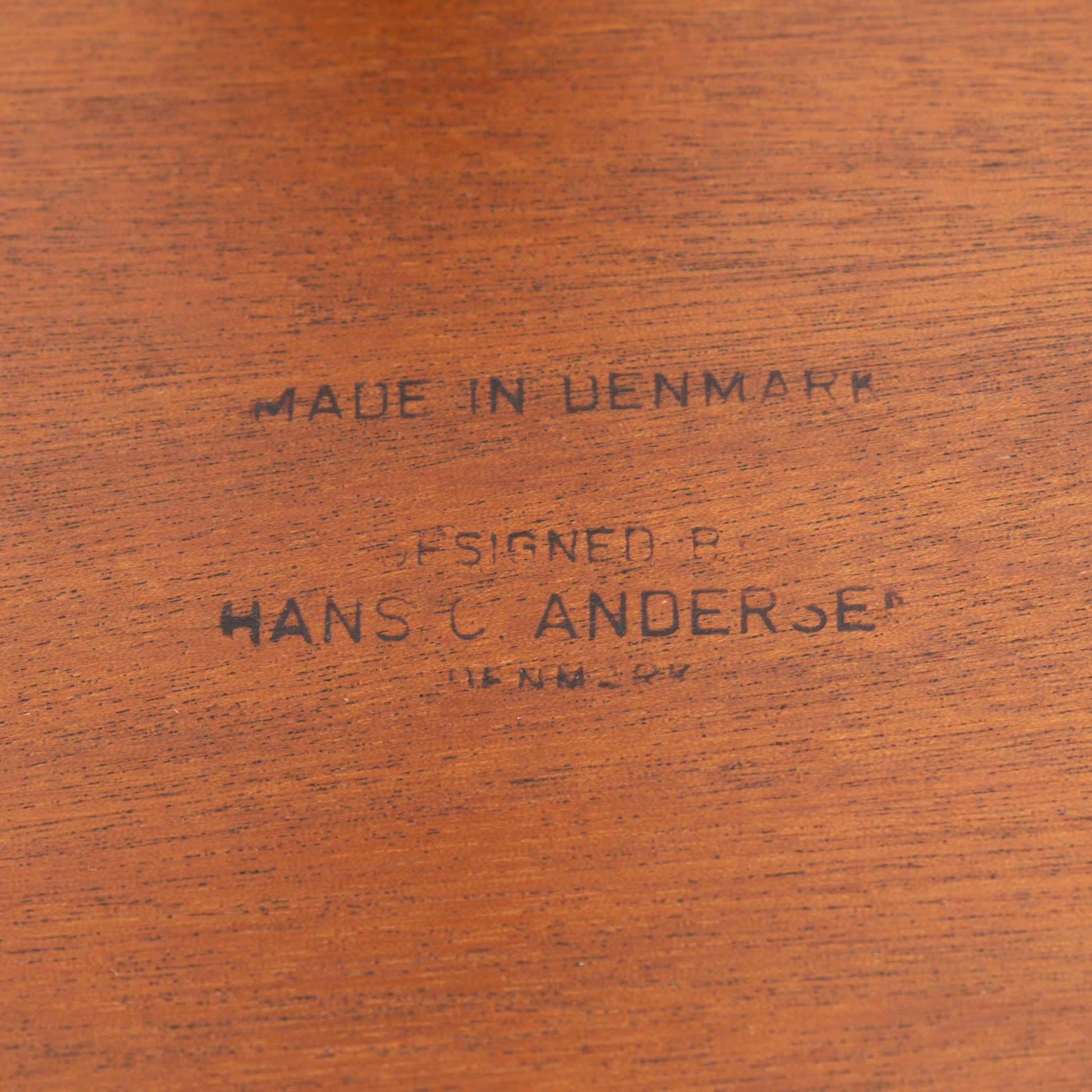 Close-up of the maker’s mark stamped on smooth teak wood, indicating the Hans Andersen Teak Tripod Side Table’s authentic Danish mid century modern origin.