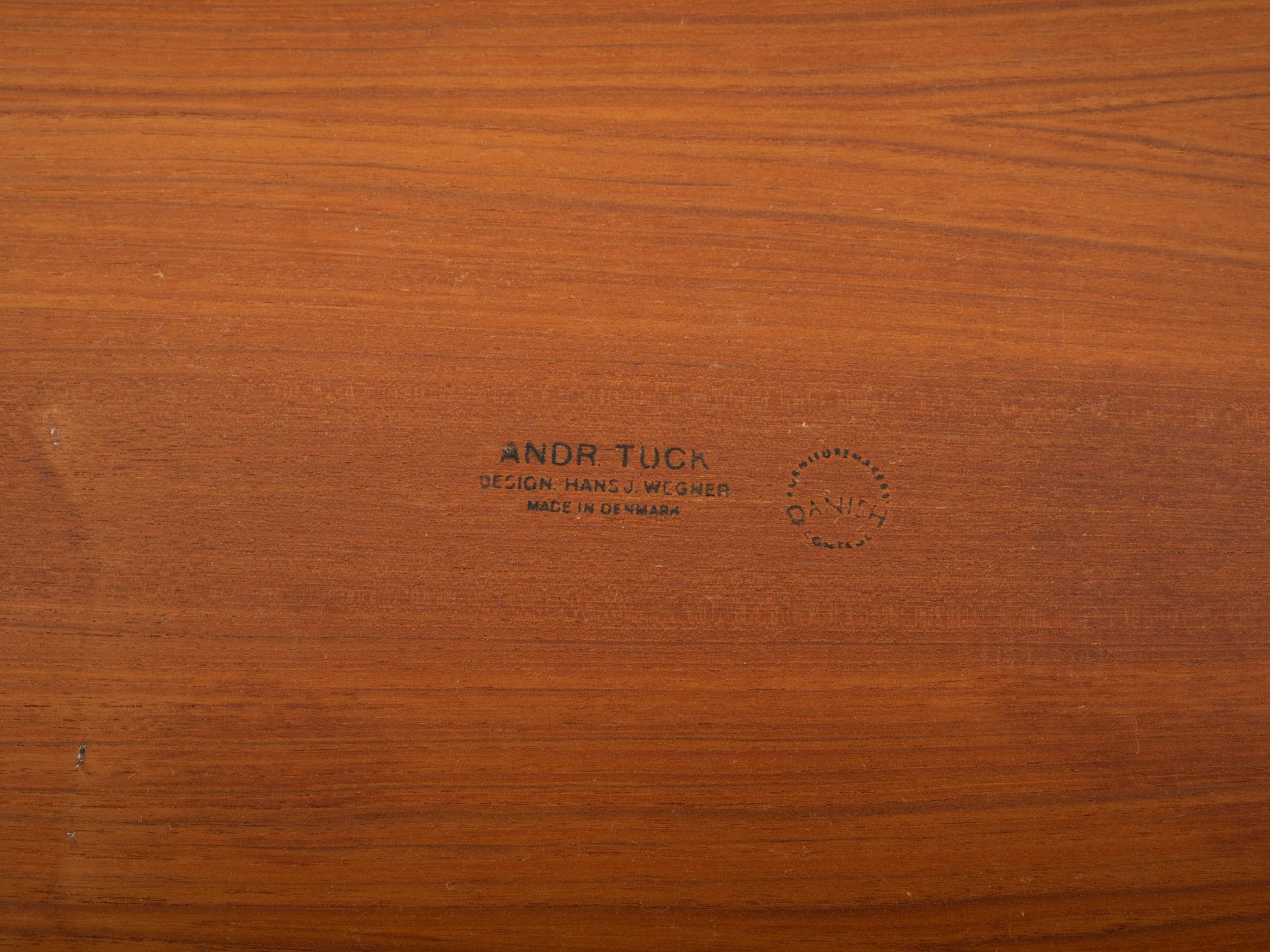 Close-up of teak wood surface with Andreas Tuck and Hans J. Wegner designer stamps on mid-century modern furniture piece