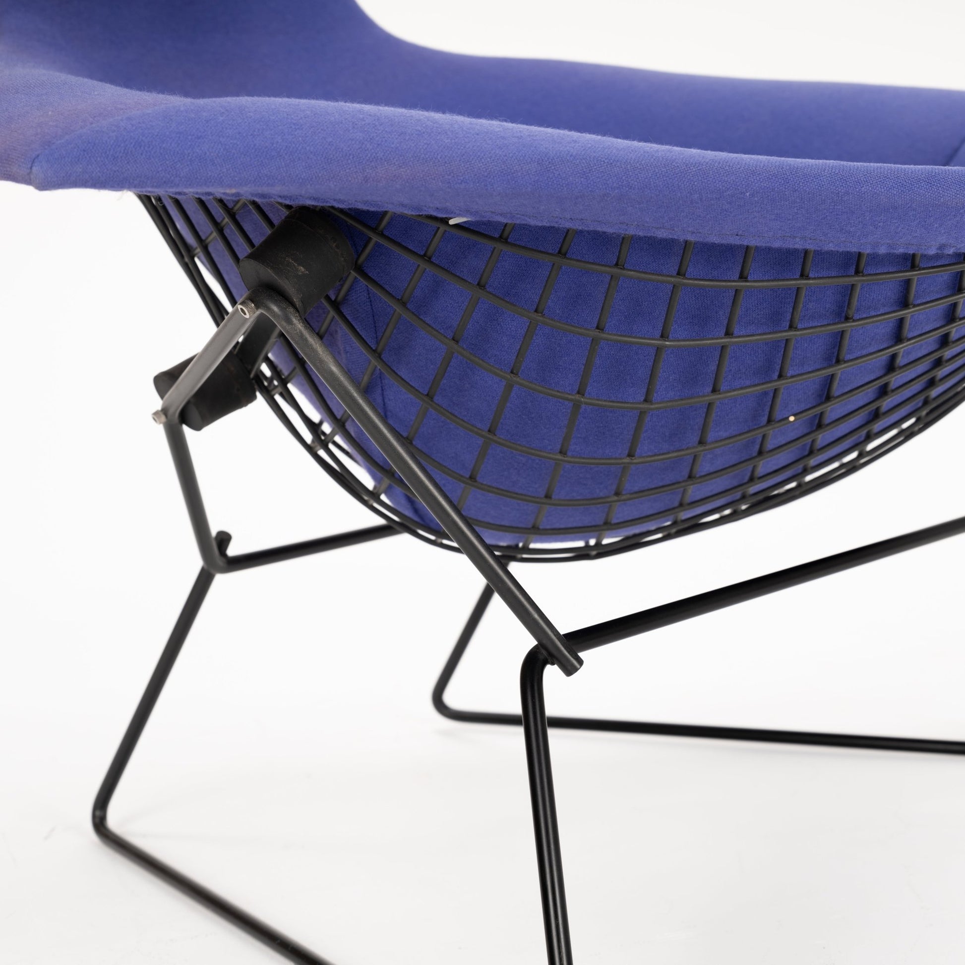 Close-up of a black wireframe lounge chair with a contoured blue fabric seat and angled metal supports