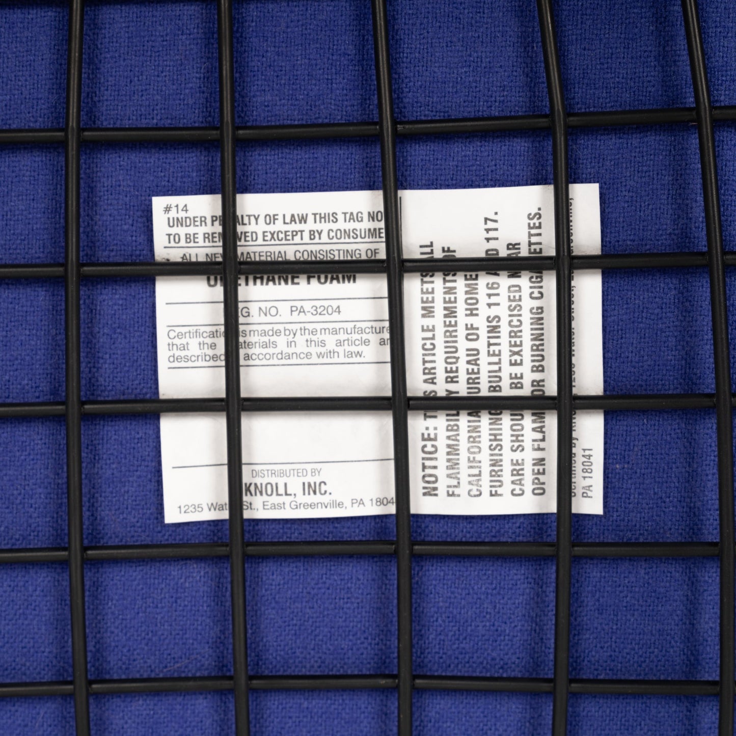 Close-up of a white product tag under a black wire grid on a textured deep blue fabric surface