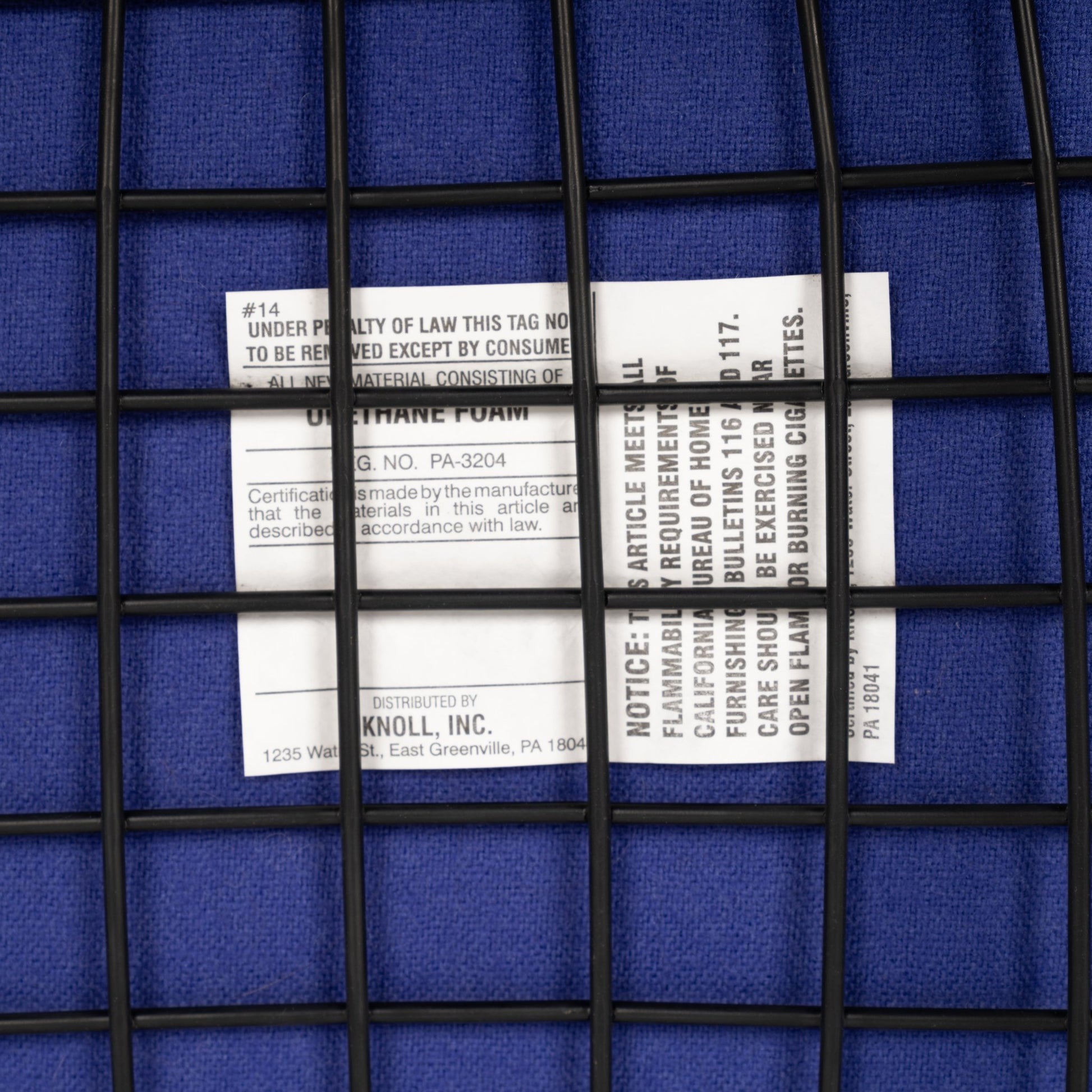 Close-up of a white product tag under a black wire grid on a textured deep blue fabric surface