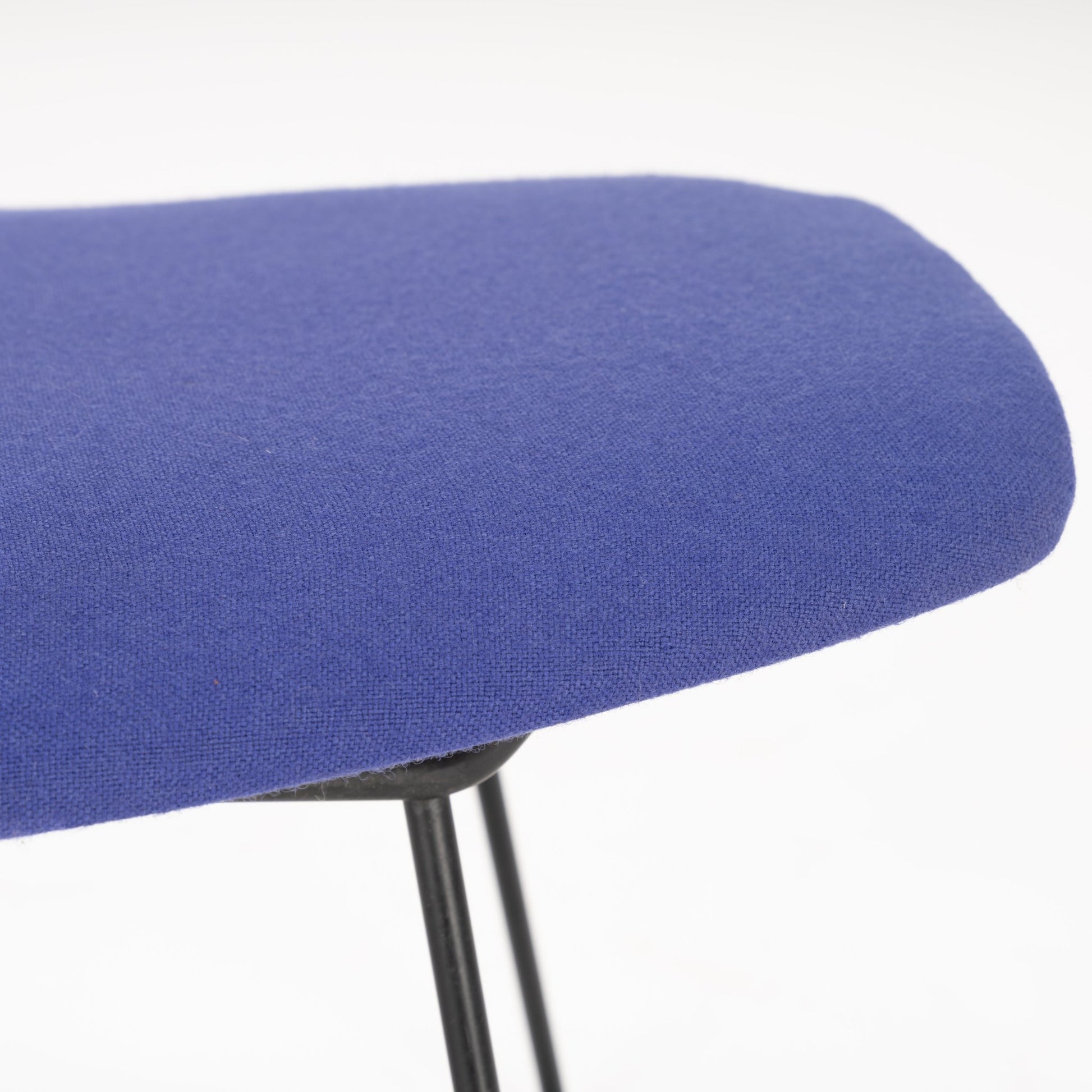 Close-up of a smooth blue fabric seat with rounded edges on a slender black metal stool frame against white background