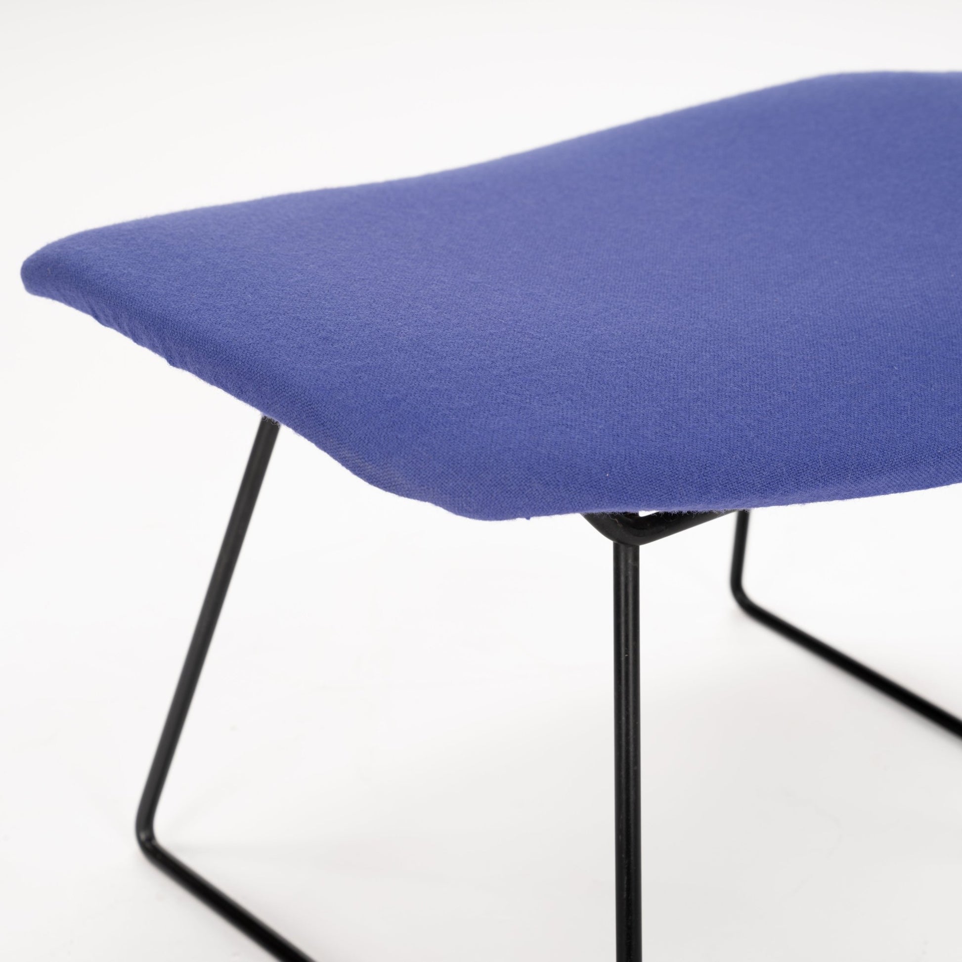 Close-up of a low-profile stool with smooth purple fabric seat and slender black metal legs against white background