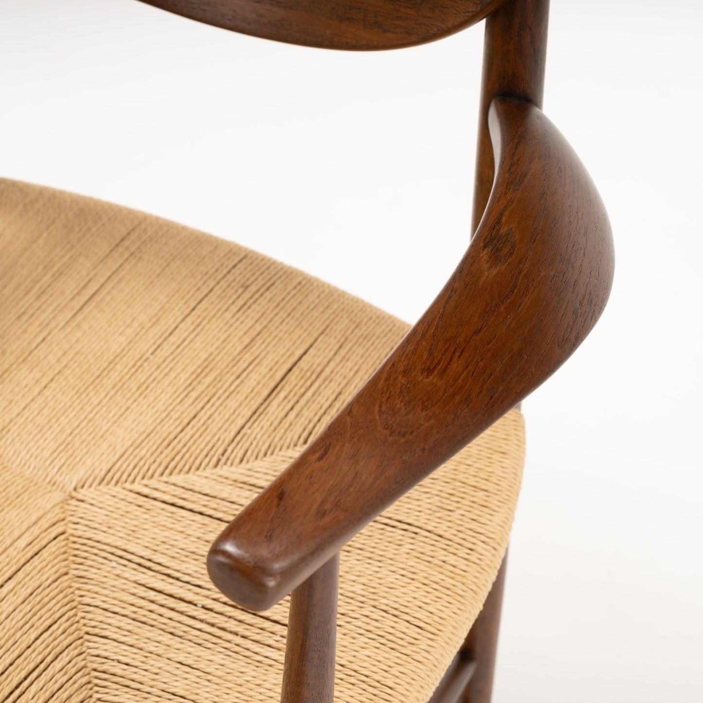 Close-up of Hvidt & Molgaard Model 317 chair’s sculpted curved teak armrest and woven natural fiber seat detail