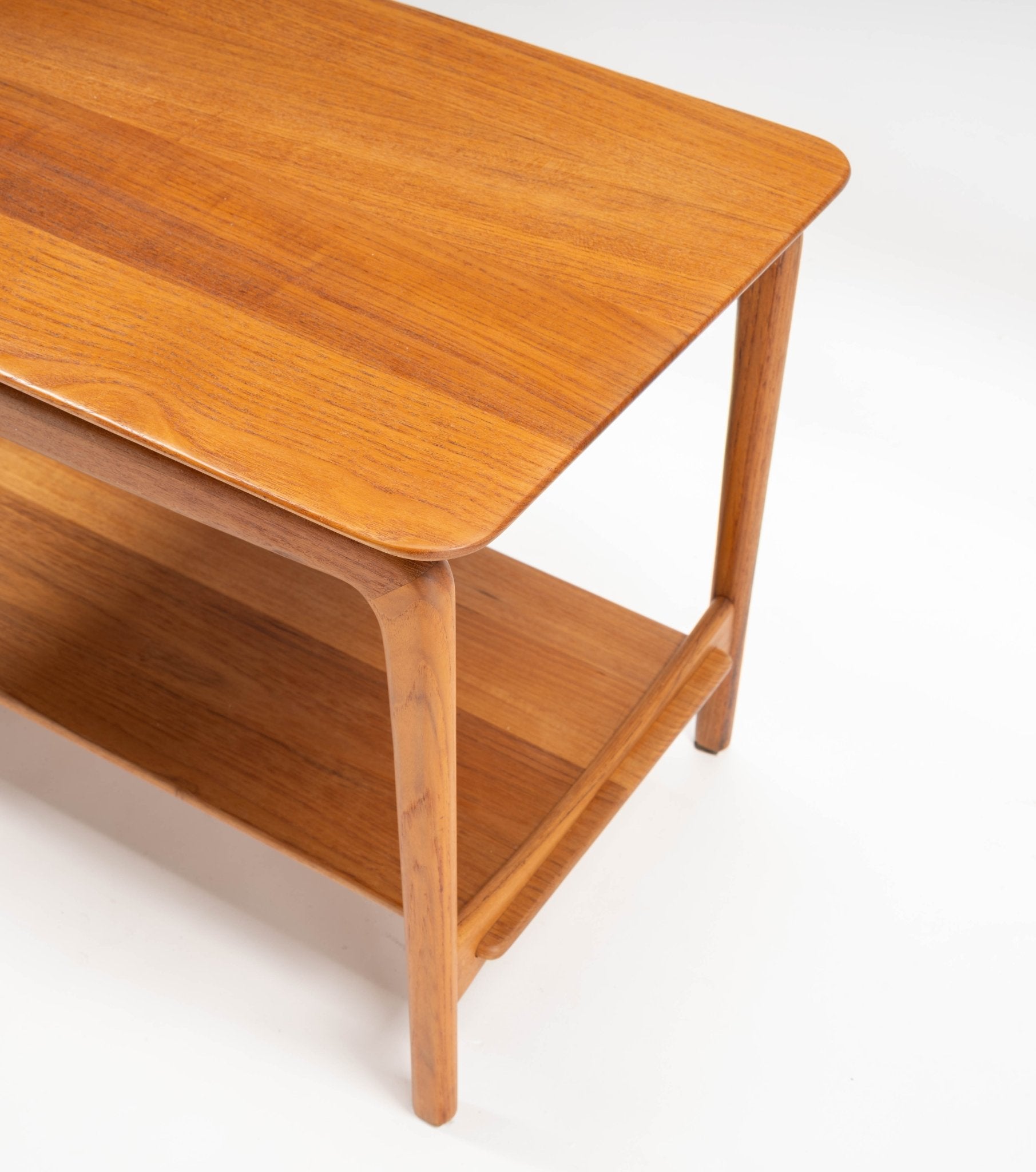 1950s Danish mid-century modern teak side table with sculpted legs and lower shelf on white background