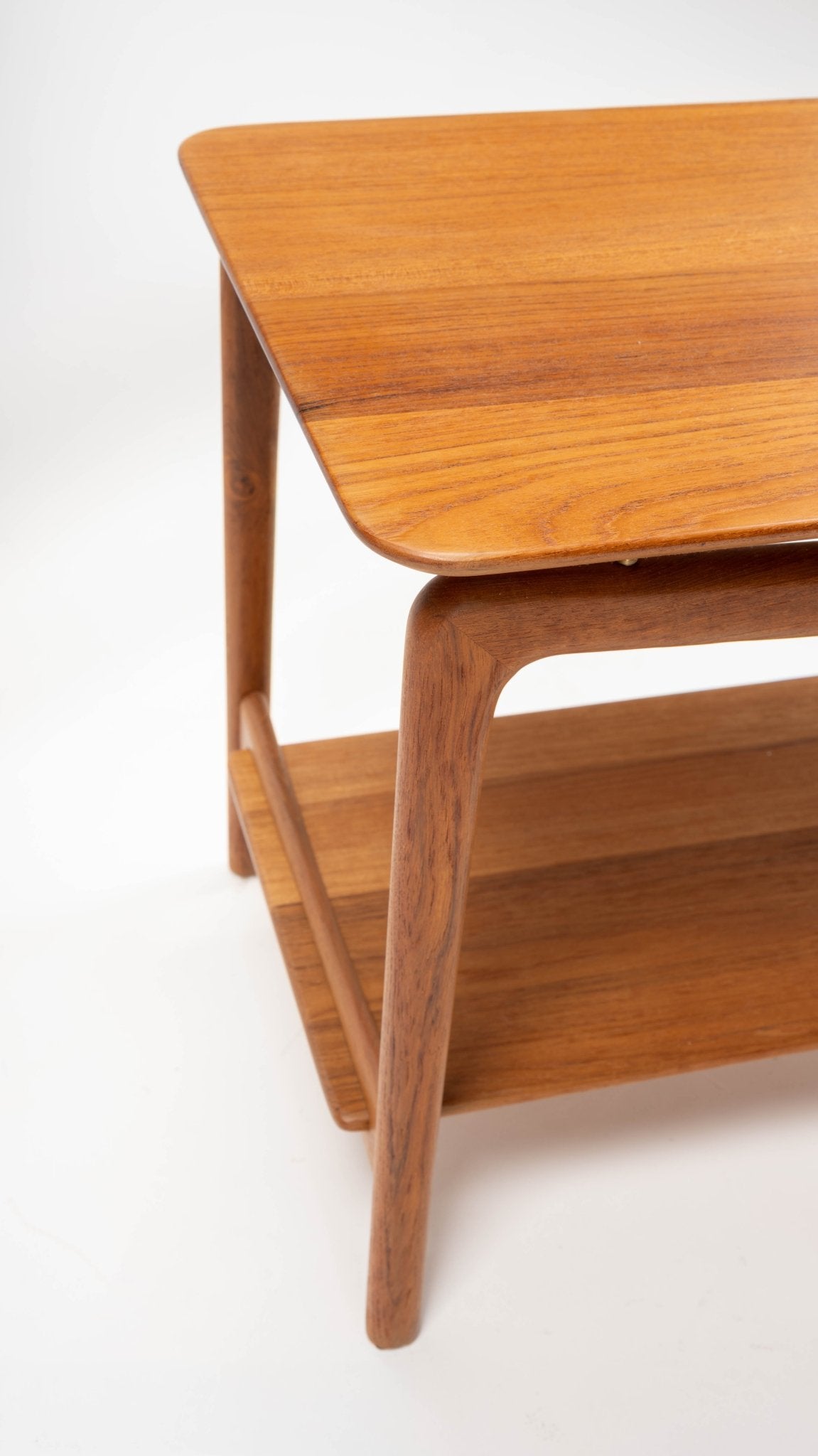 Close-up of mid-century modern teak side table with sculpted legs and rounded edges on white background