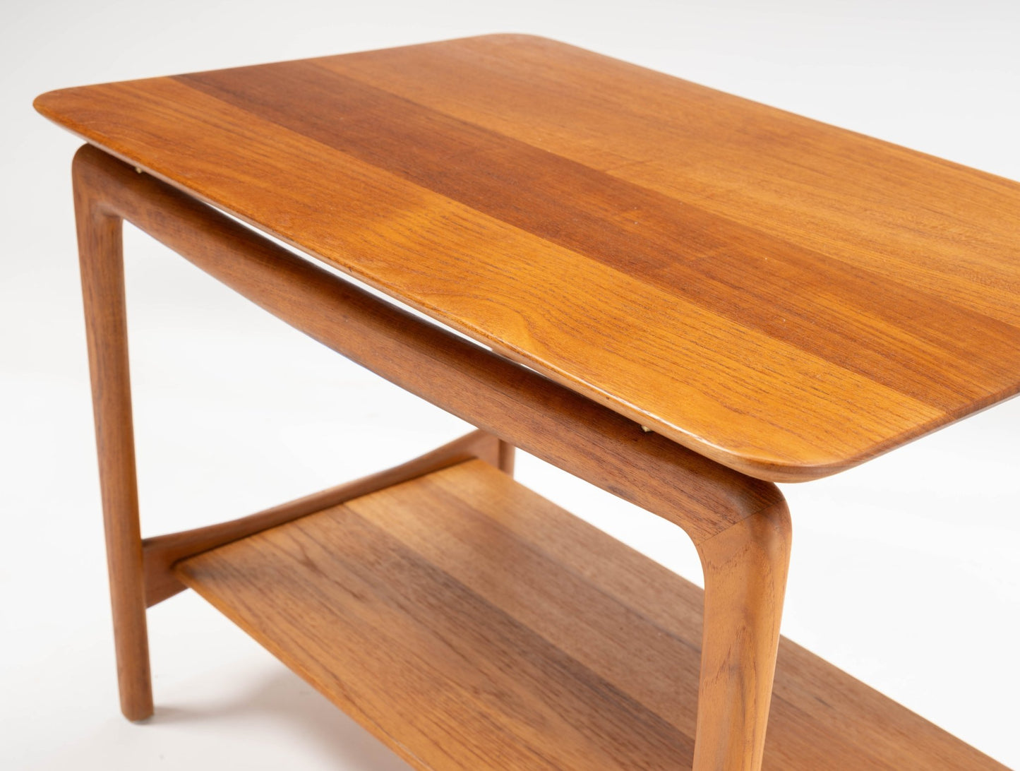 Mid-century modern teak side table by Hvidt & Molgaard with sculpted legs and lower shelf on white background.