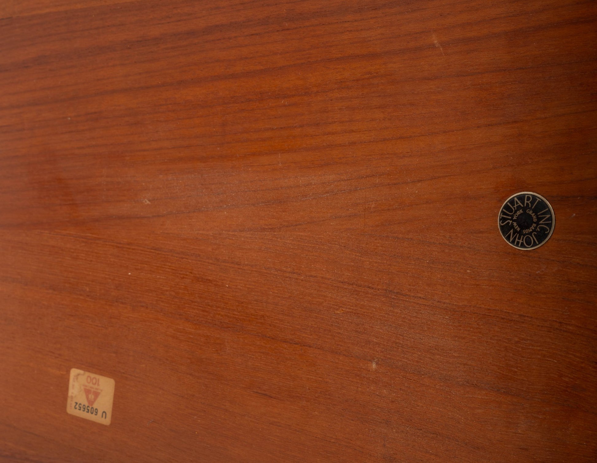 Close-up of mid-century modern teak tabletop with circular manufacturer label and rectangular vintage sticker.