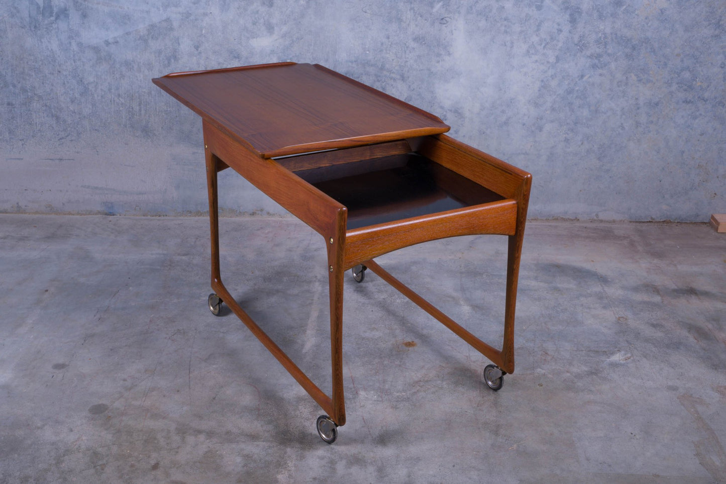 1960s Danish teak bar cart with sliding top revealing black laminate storage compartment on casters