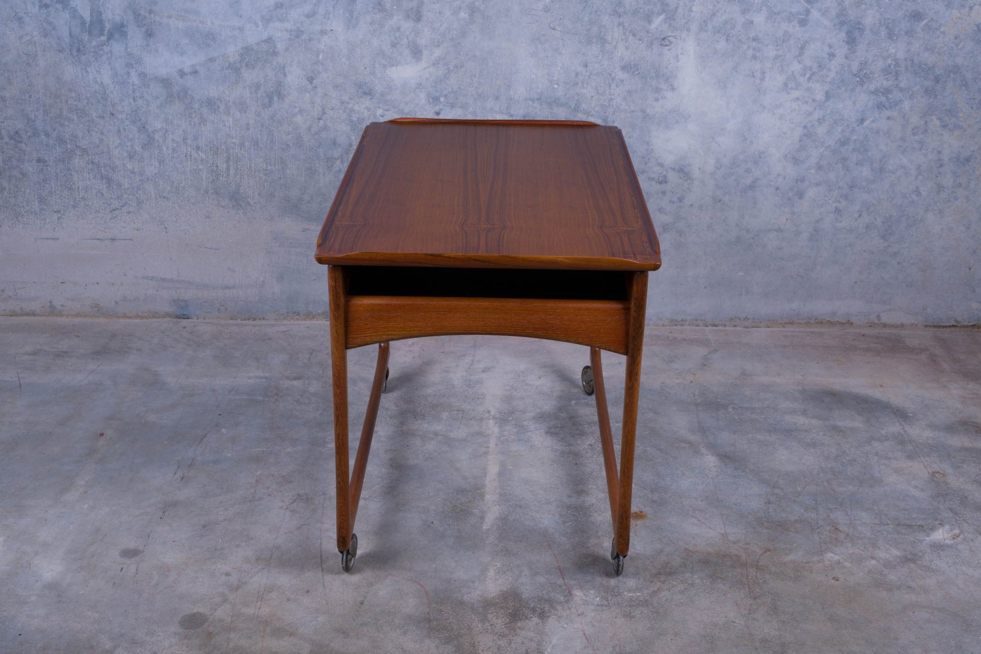 Ingvar Jensen teak bar cart with sliding top, storage compartment, tapered legs, and rolling casters on concrete floor