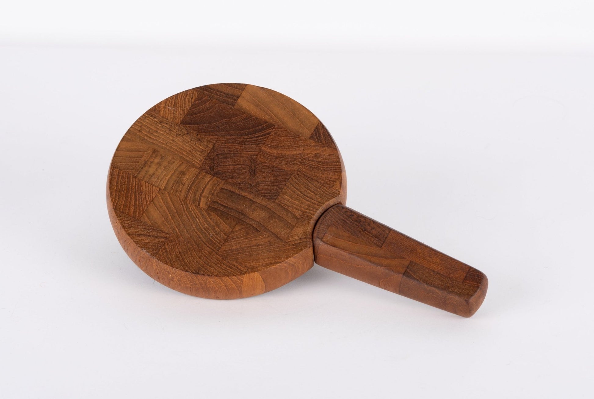Round mid-century modern teak cutting board with integrated handle and butcher block design on white background.