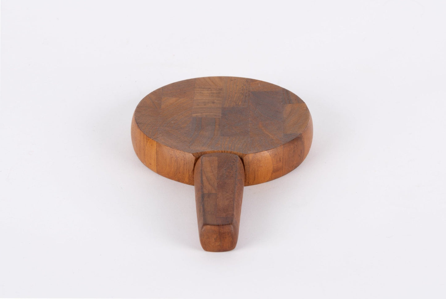 Round mid-century modern teak cutting board with butcherblock design and integrated handle on white background