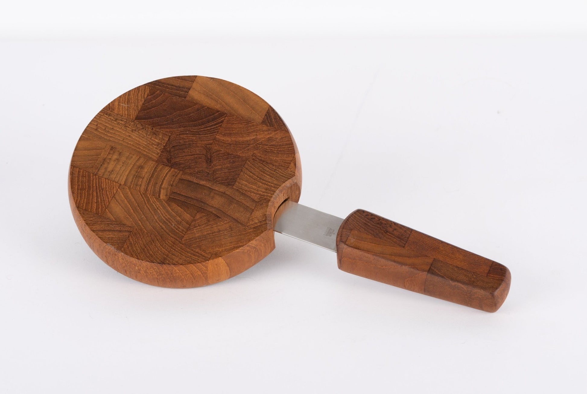 Round mid-century modern Jens Quistgaard teak cutting board with integrated knife and butcherblock design on white background