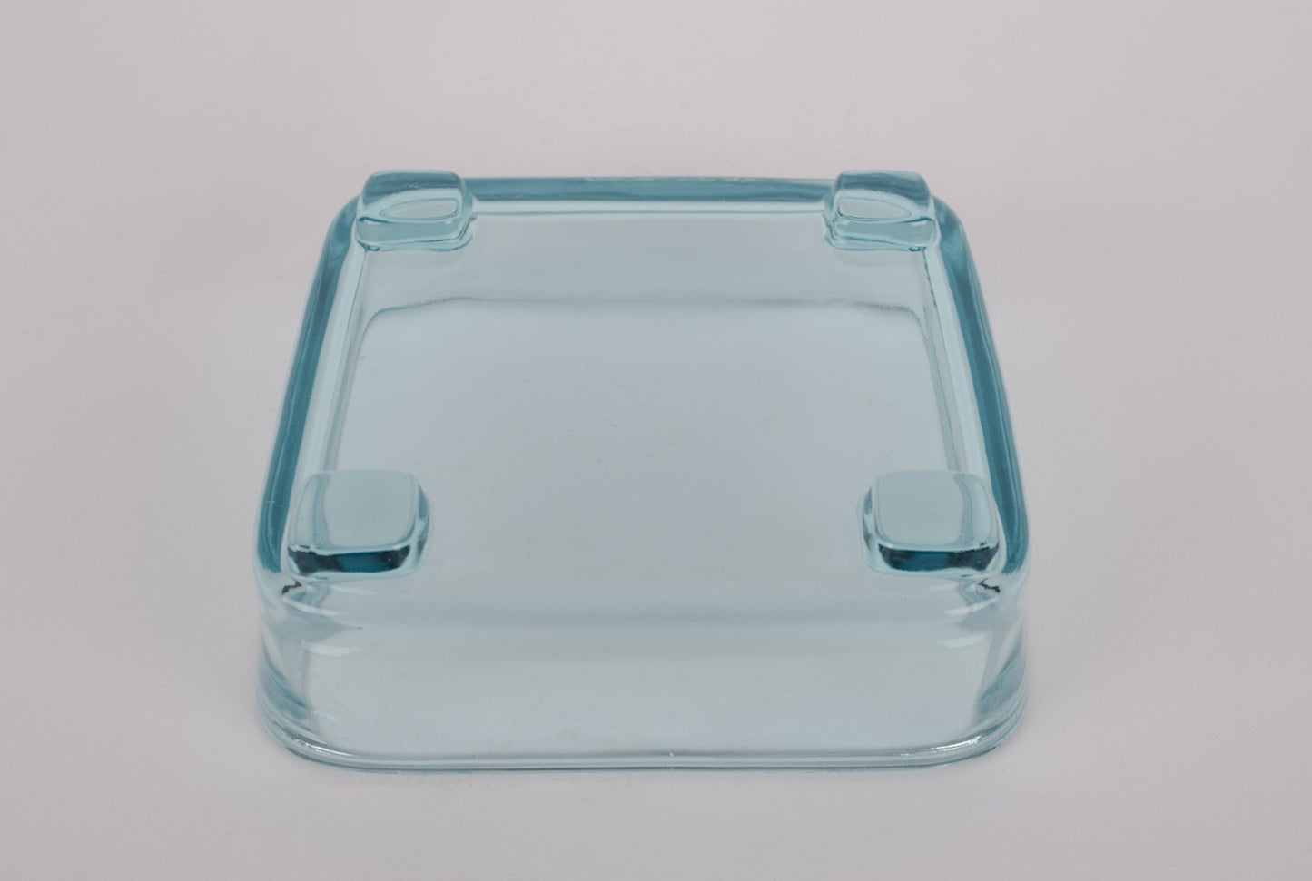 Square mid-century modern clear glass dish with raised feet on white background.