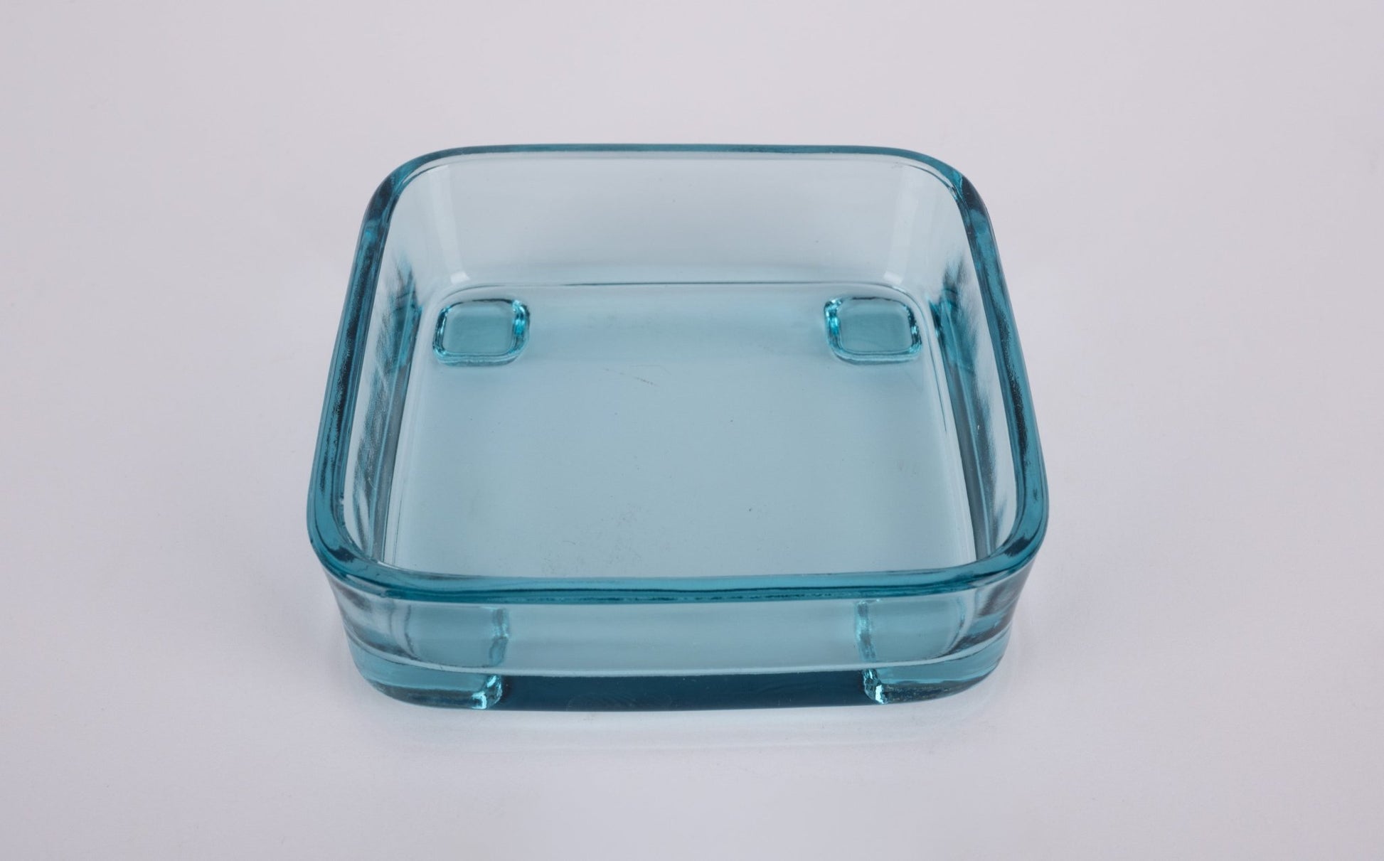 Square light blue glass insert bowl with rounded corners and raised feet on white background