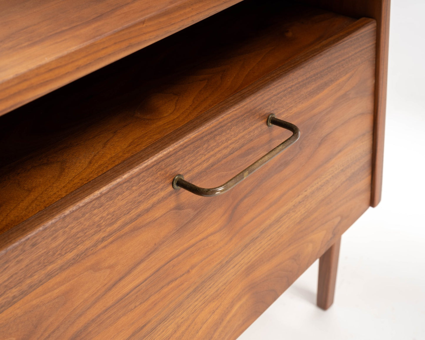 Close-up of 1960s Jens Risom walnut bedside table drawer with brass handle and open storage compartment above.