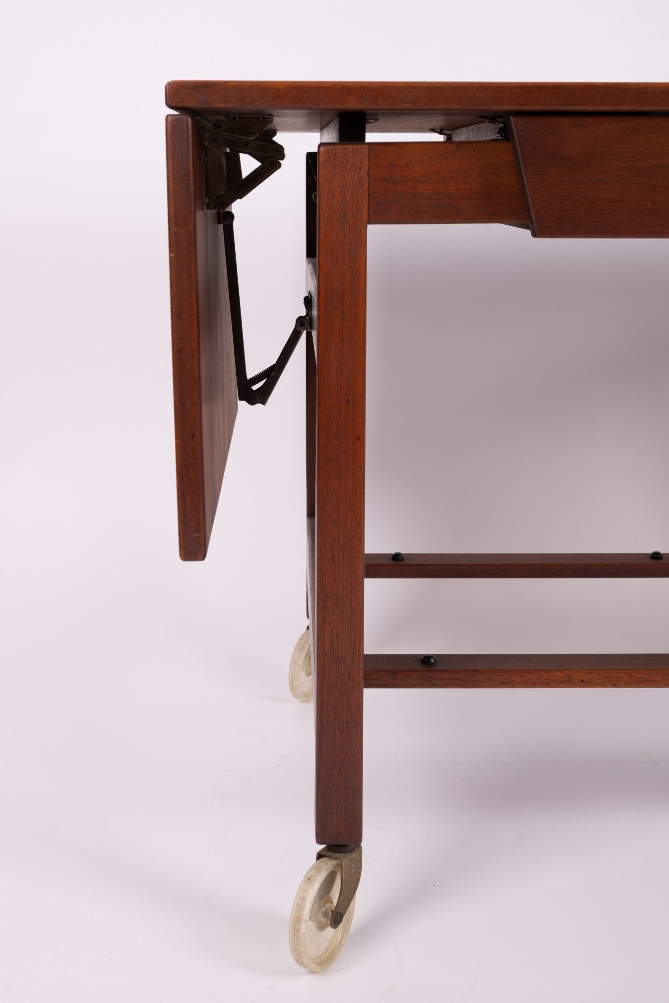 Close-up of the leg and expandable leaf mechanism on a 1960s Jens Risom wooden serving cart with caster wheels