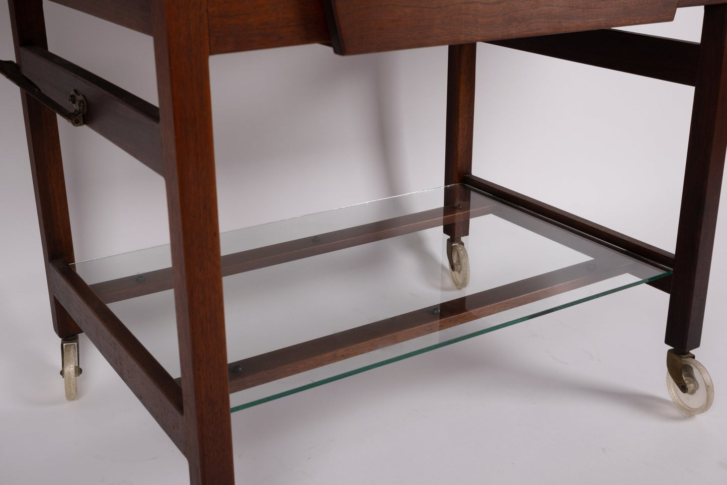Lower section of Jens Risom 1960s expandable serving cart with wooden frame and glass shelf on caster wheels