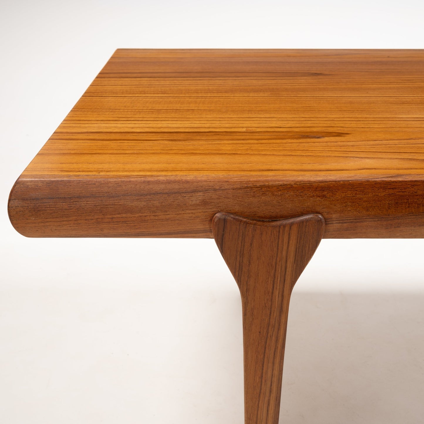 Close-up of teak coffee table corner showing smoothly rounded edge and tapered leg in Danish mid-century modern style