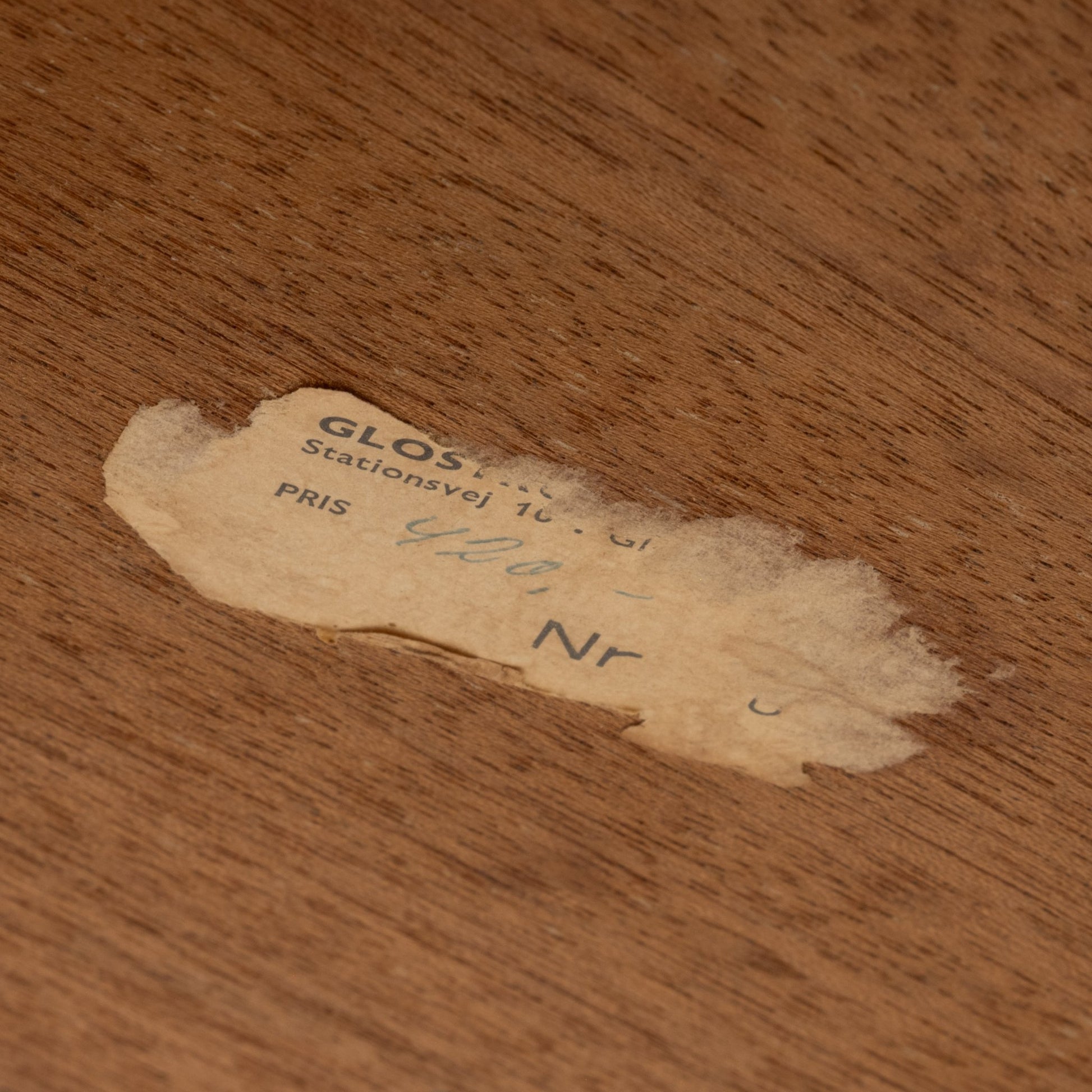 Close-up of aged price label partially peeled on smooth teak surface of Johannes Andersen Danish mid-century coffee table