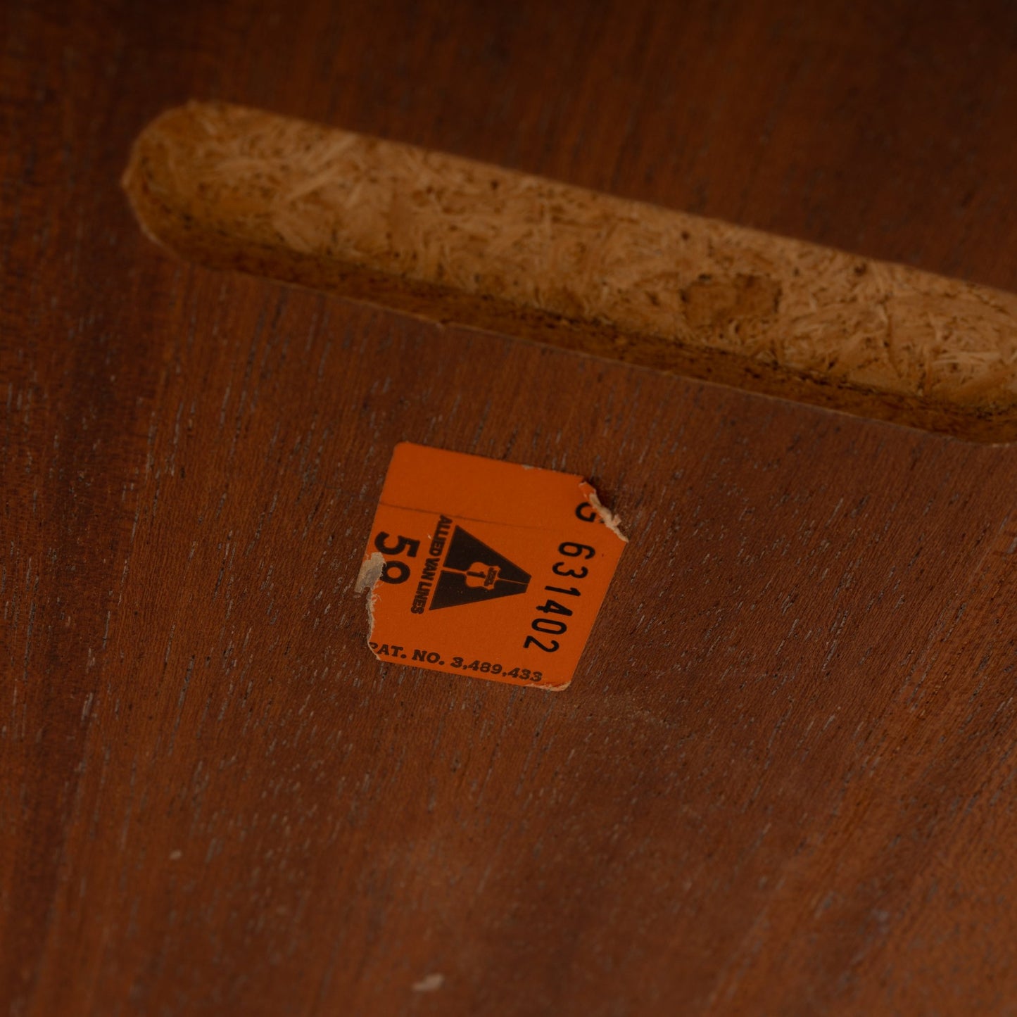 Close-up of wooden furniture underside with an orange vintage label and a carved finger pull handle in a dark finish