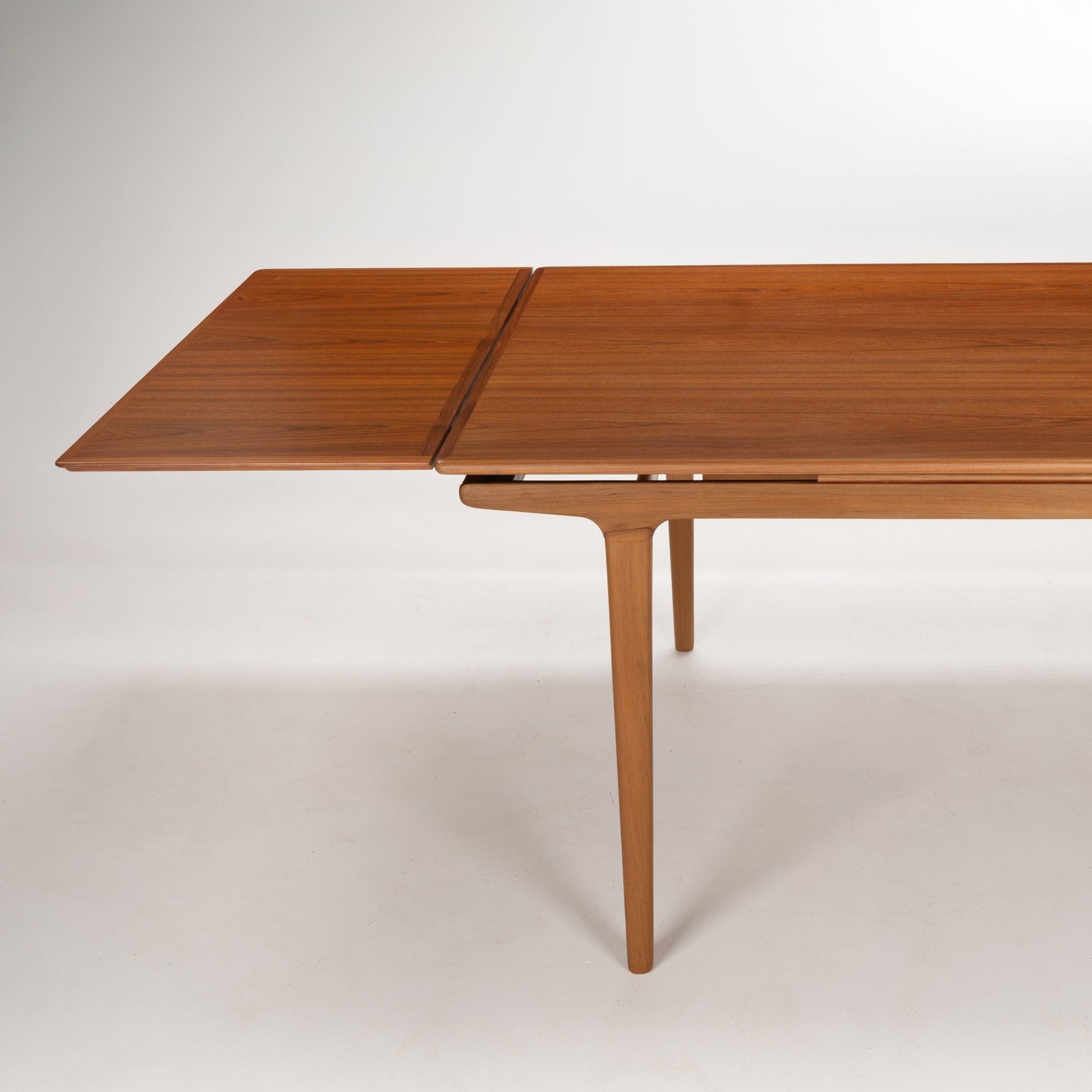 Mid-century extending wooden dining table with smooth surface and slender tapered legs in a warm walnut finish